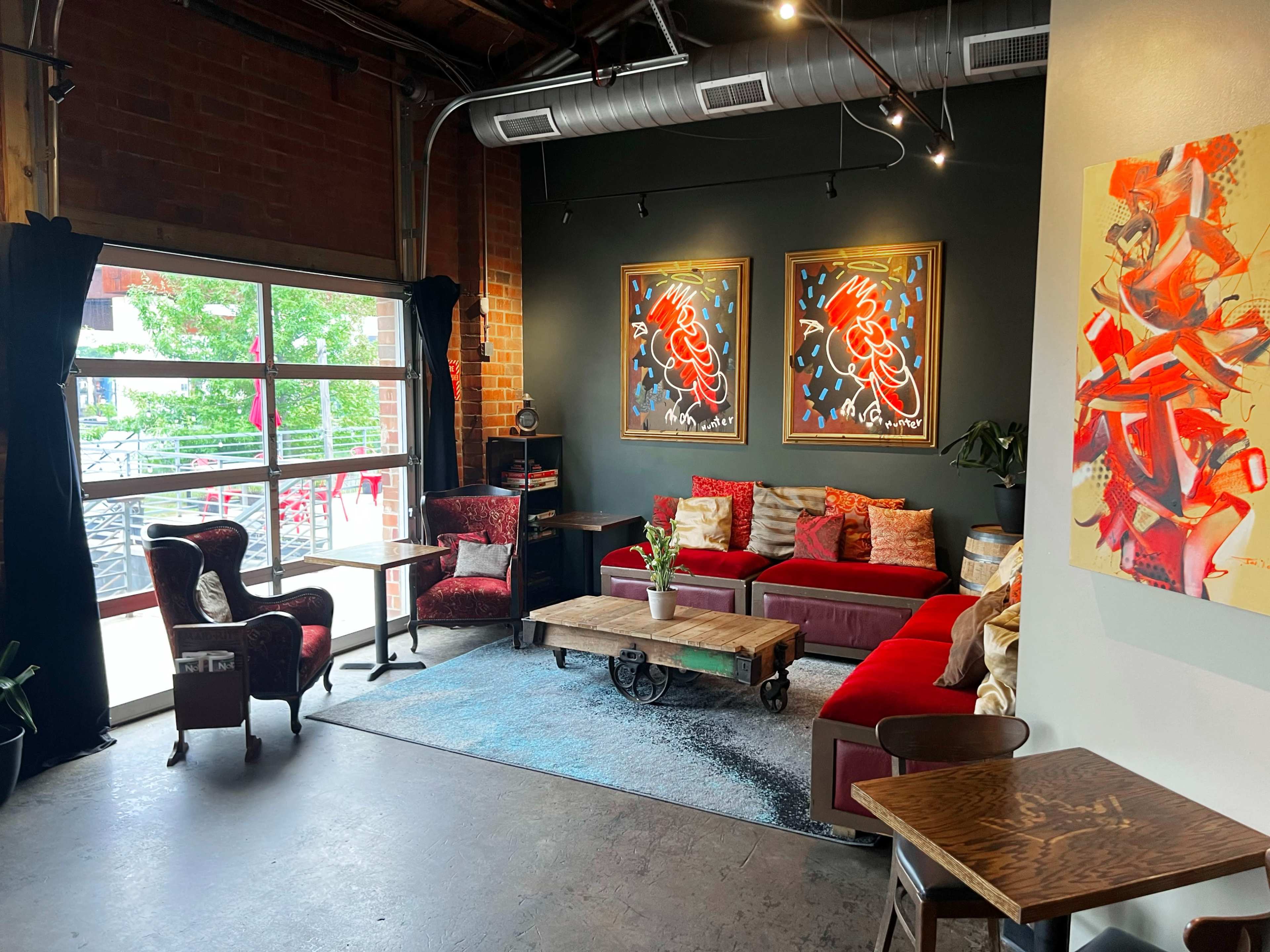 A cozy lounge area featuring a red sofa, two art pieces on a dark wall, and large windows that illuminate the space.