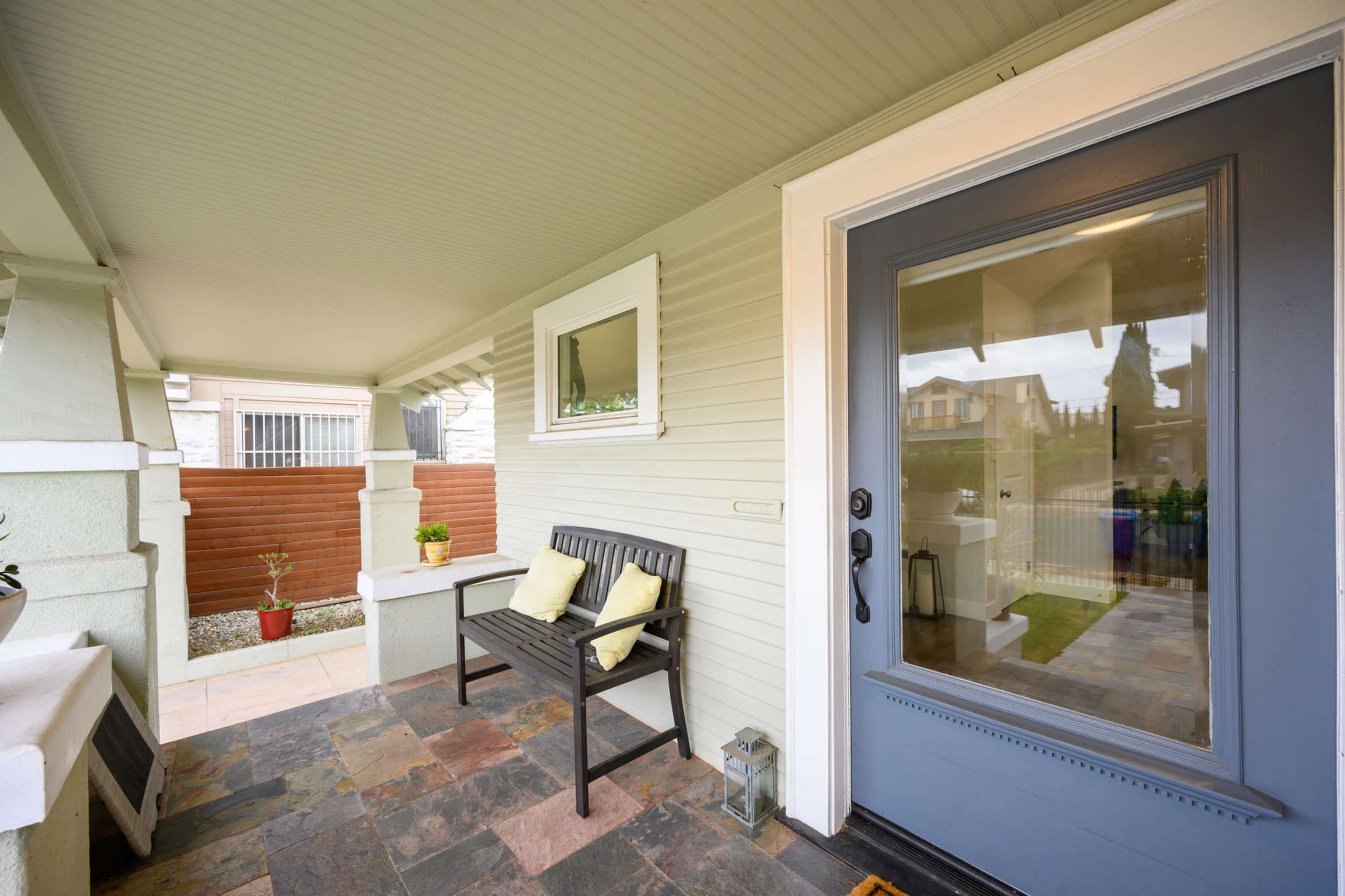 A front porch with a bench, two cushions, and a door leading inside a house.