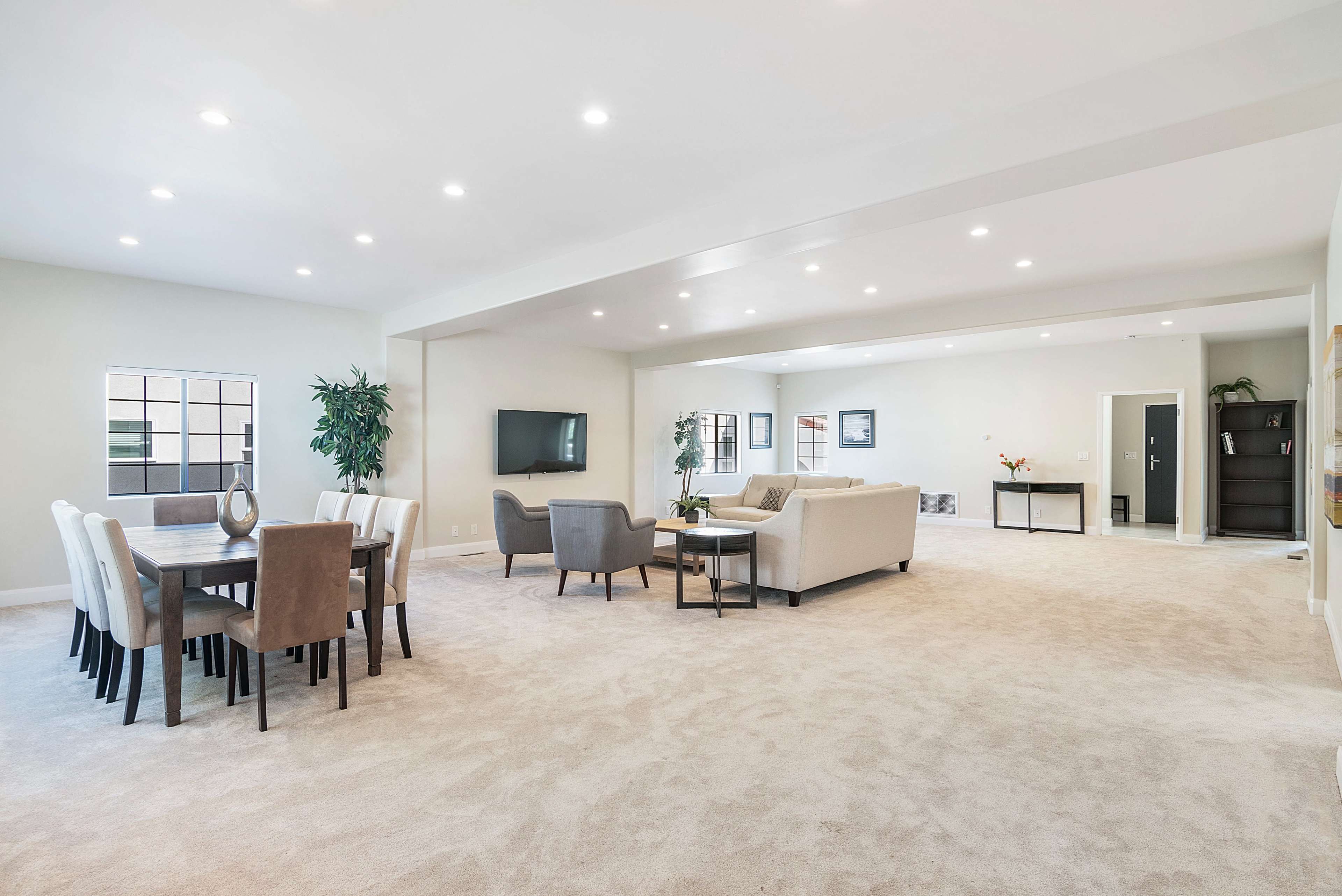 A spacious living area features a dining table, multiple seating arrangements, and large windows that allow for natural light.