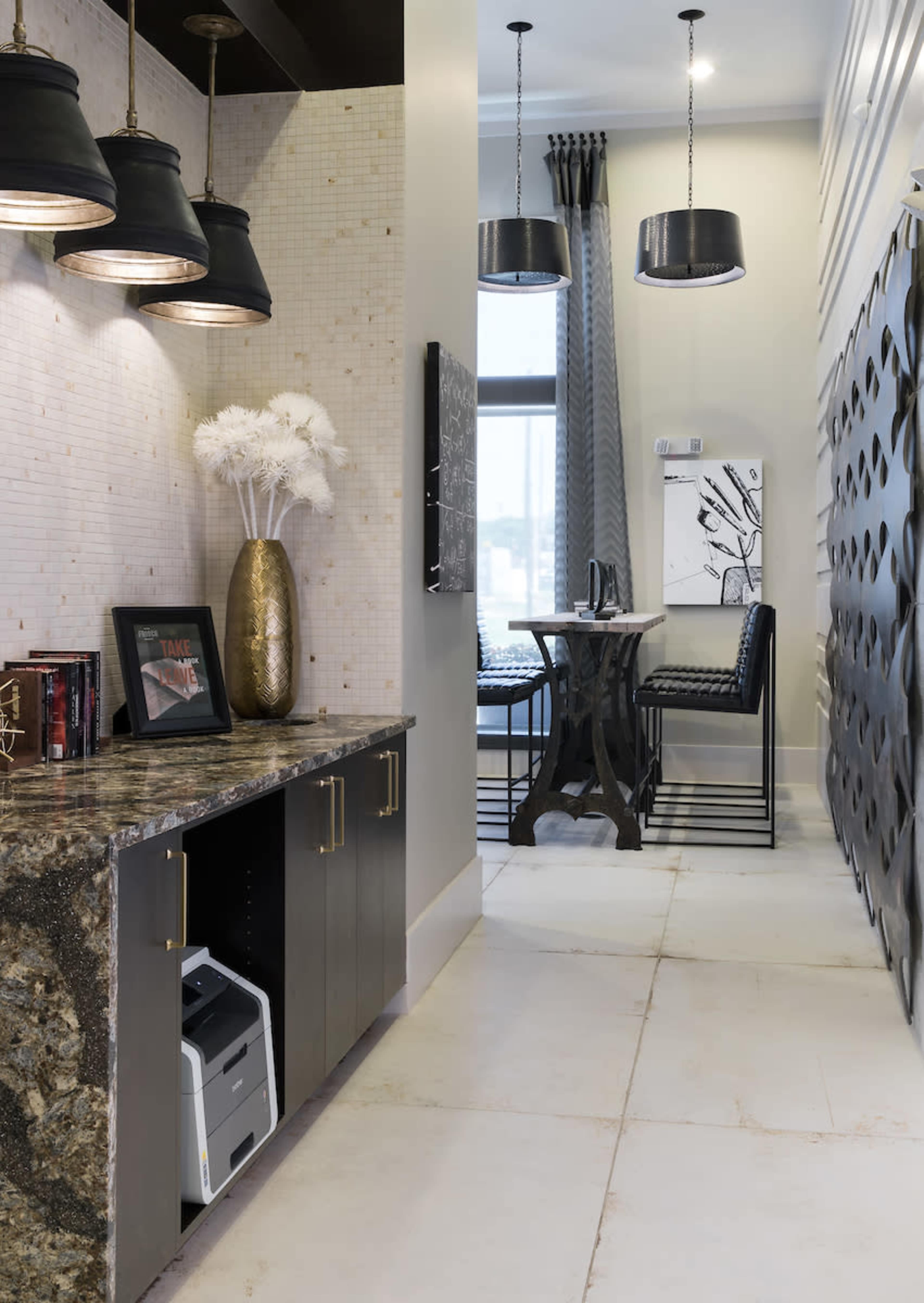 A modern hallway features a dark cabinetry with a granite countertop, leading to a seating area with tall bar stools and pendant lighting.
