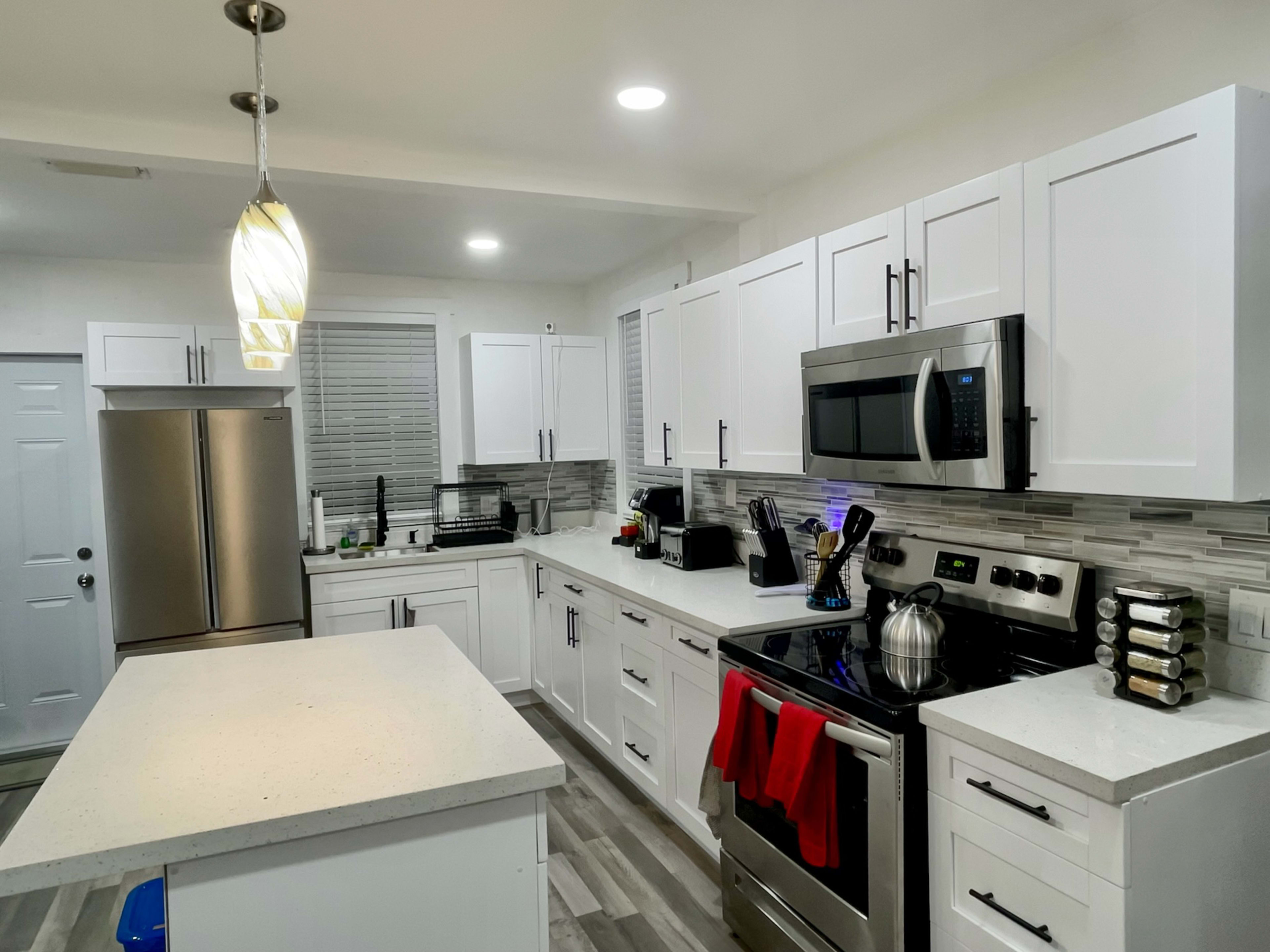 A modern kitchen features white cabinetry, stainless steel appliances, and a central island with a light fixture overhead.