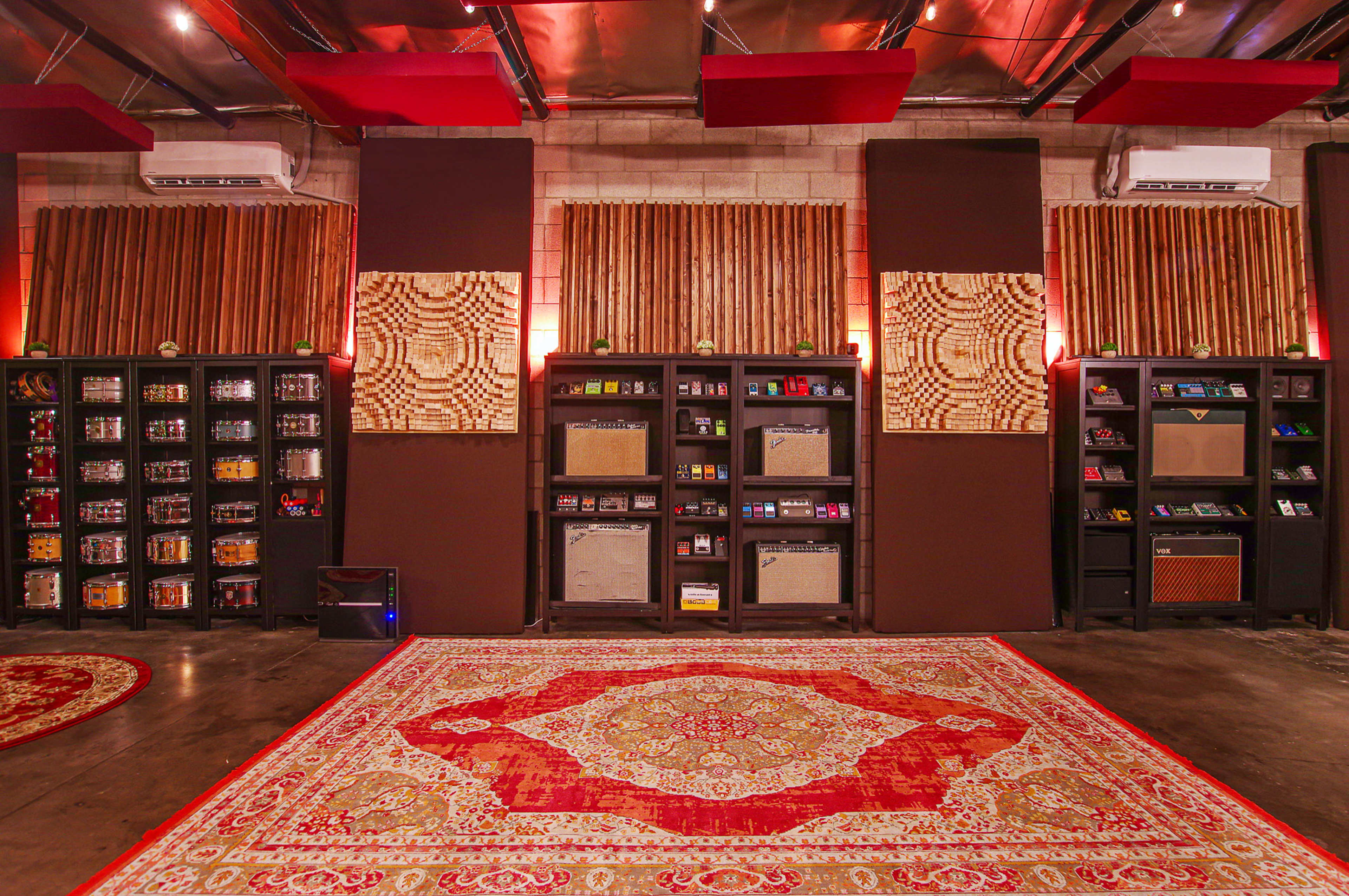 A room designed for music recording, featuring soundproofing panels, shelves filled with audio equipment, and a large decorative rug on the floor.