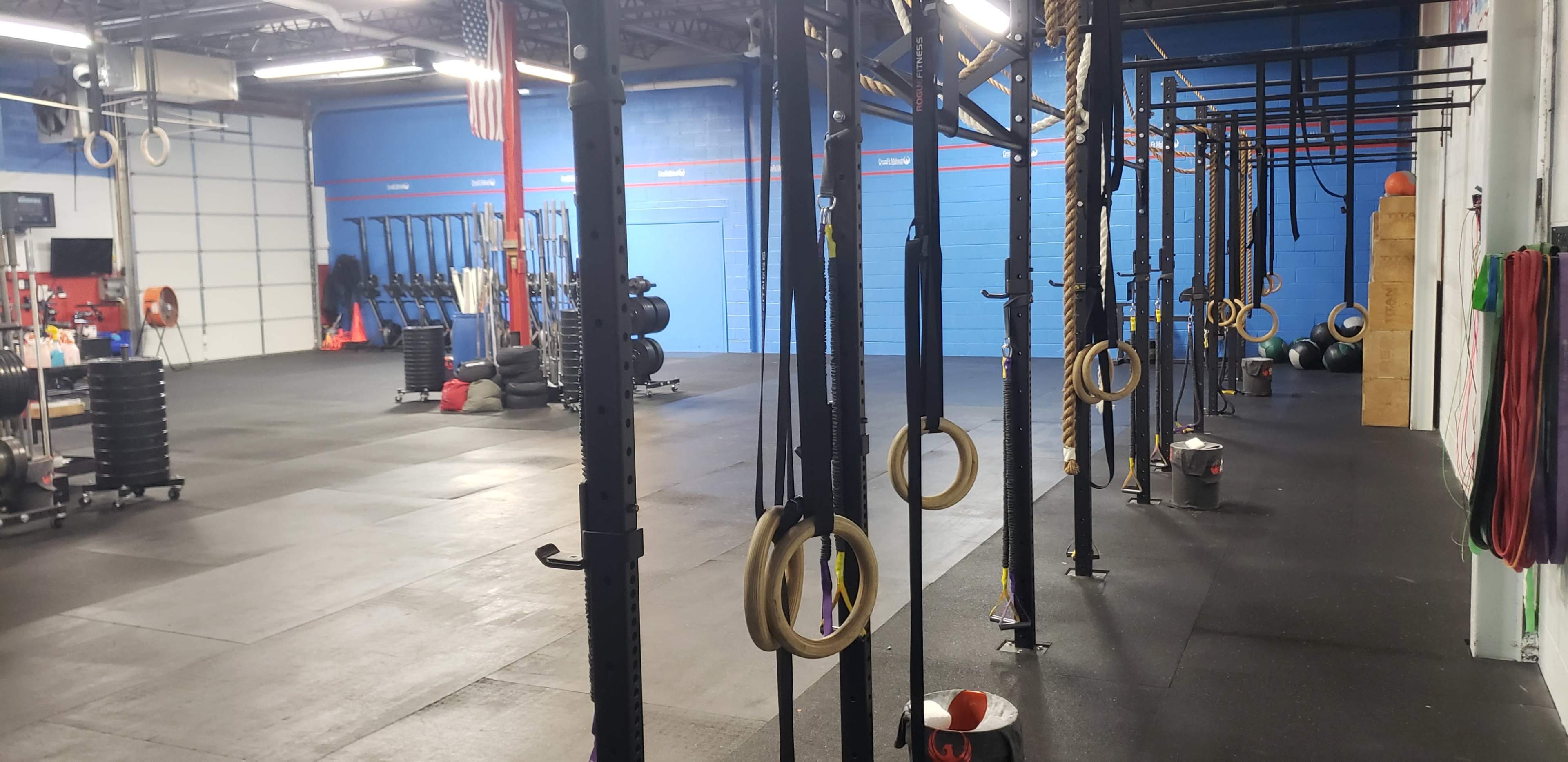 A spacious gym equipped with various exercise equipment, including weightlifting bars, fitness rings, and rubber mats.