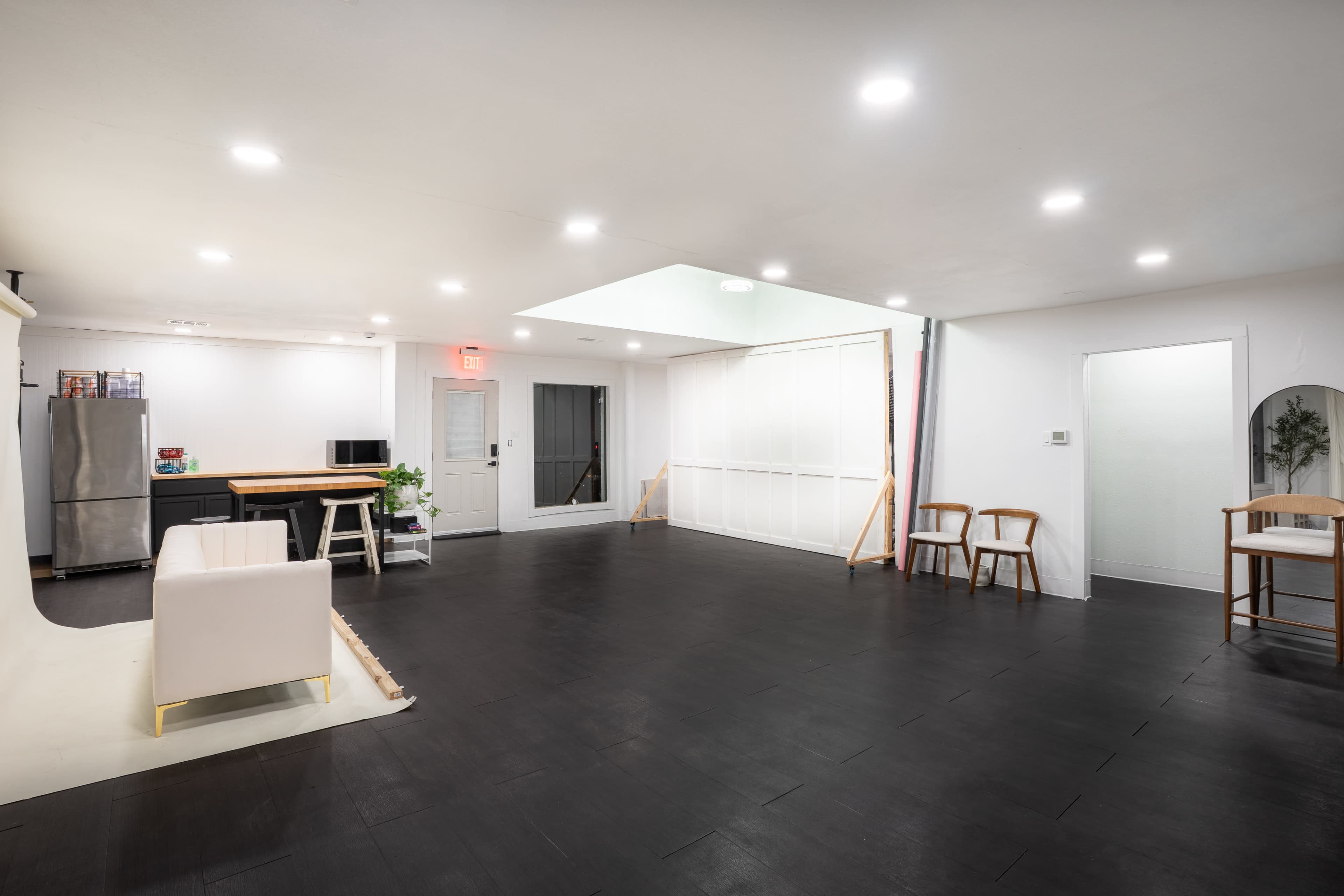 The image shows a spacious, minimally furnished room with black flooring, white walls, and several bright ceiling lights.