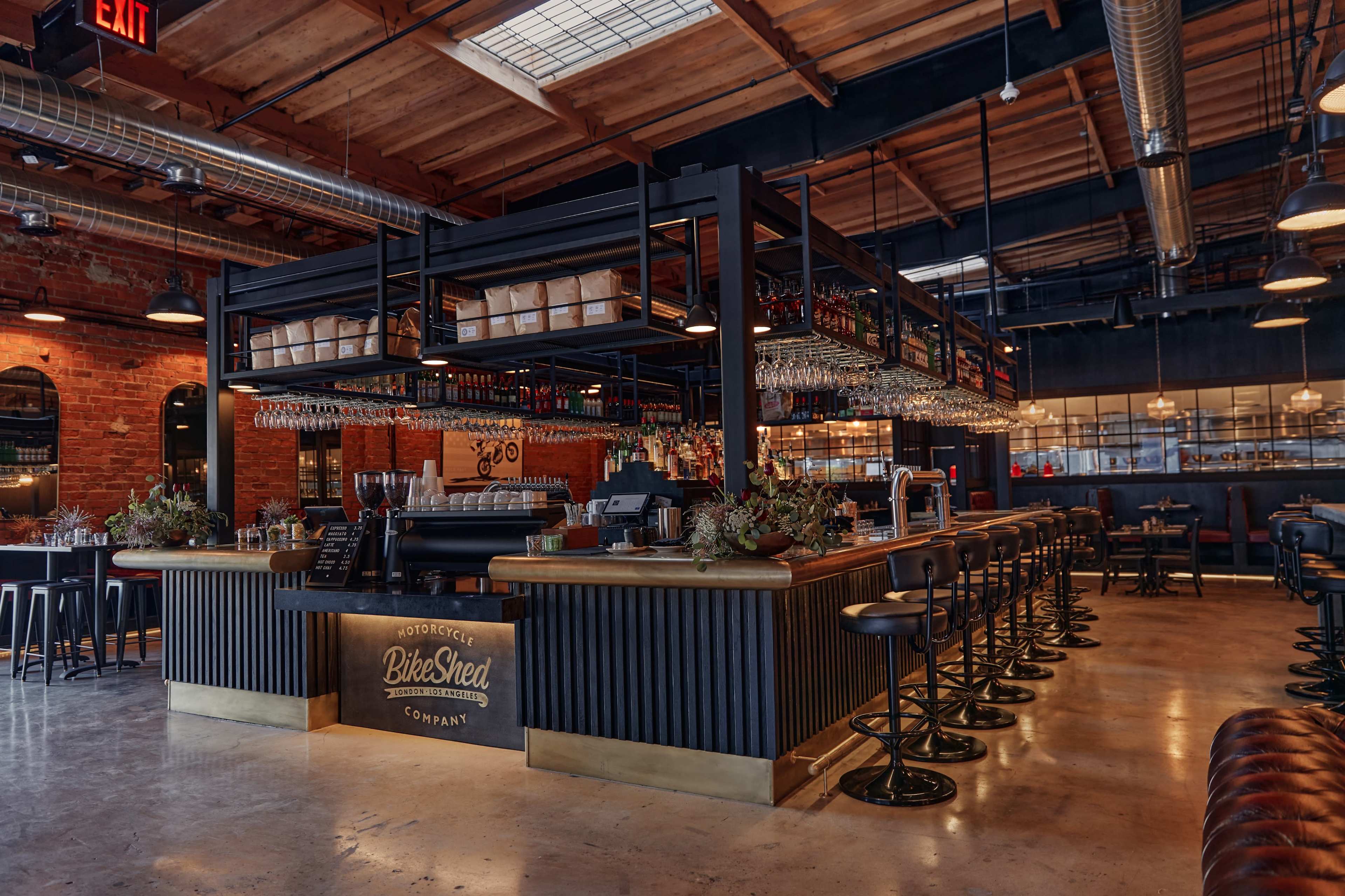 A modern bar area with a wooden counter, high stools, and a background of exposed brick walls and industrial-style lighting.
