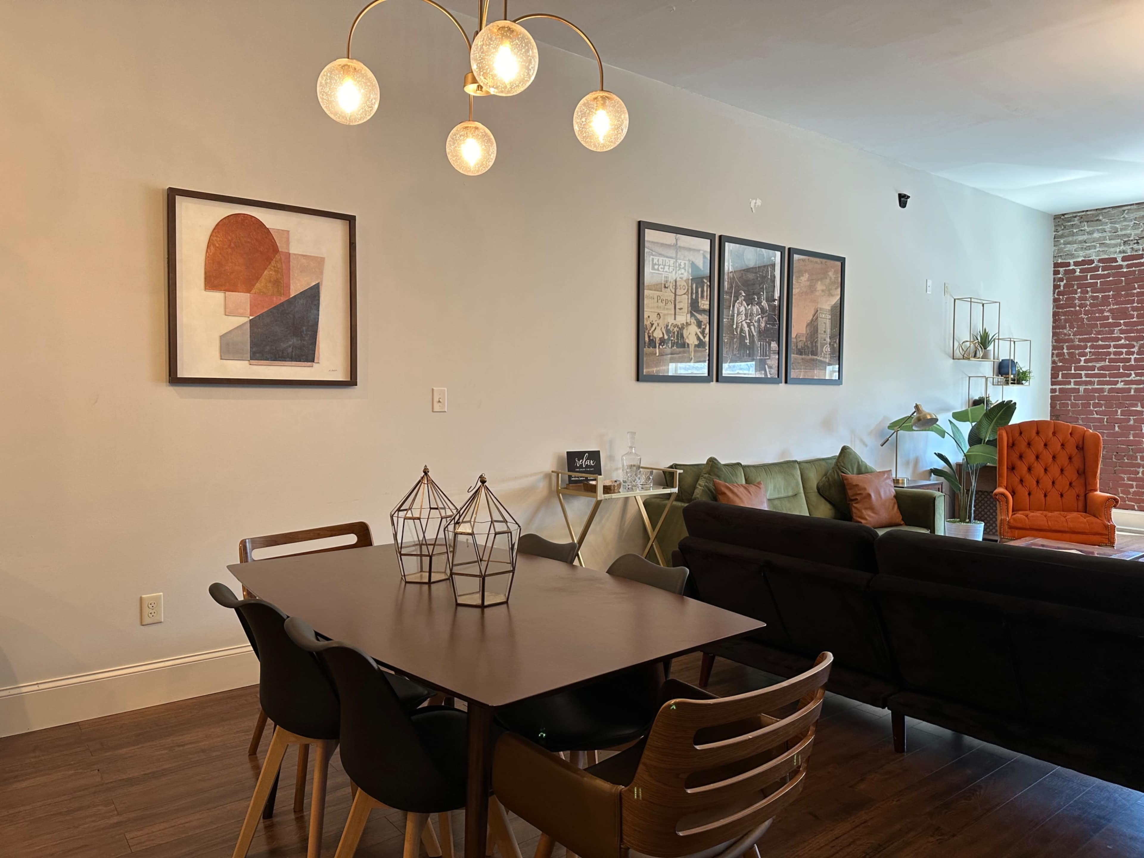 A modern living space featuring a dining table surrounded by chairs, a green sofa, an orange armchair, and framed artwork on the wall.