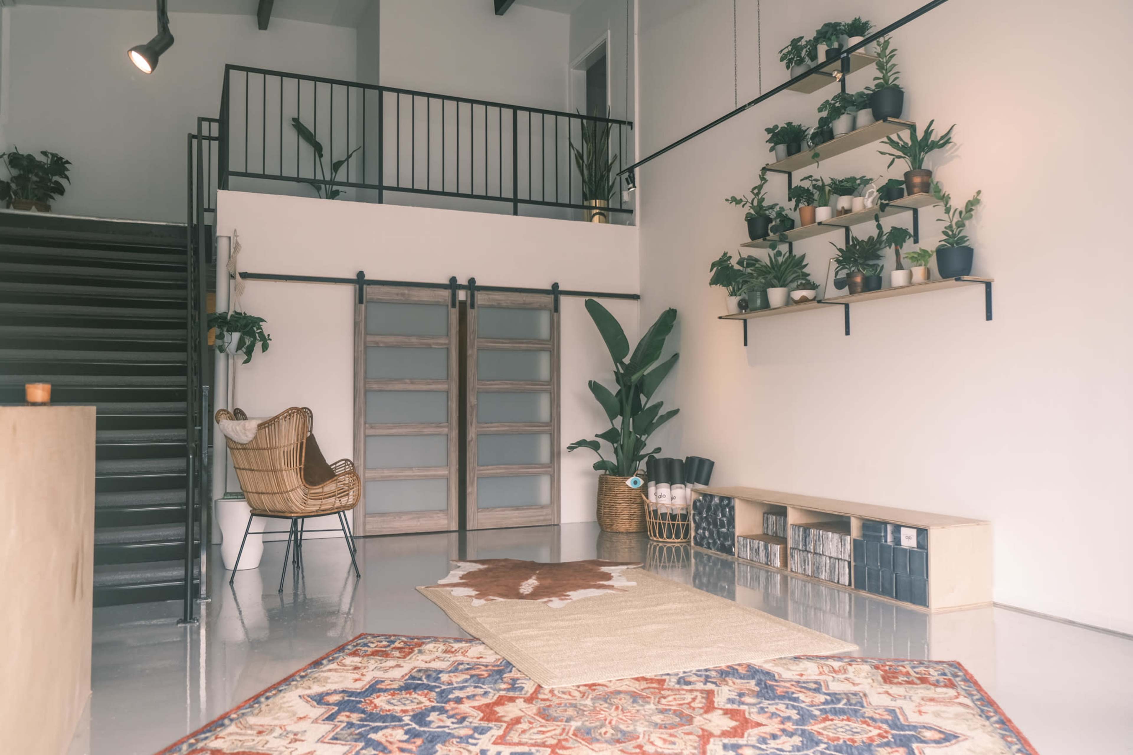 A modern interior with a staircase, a seating area, and shelves filled with potted plants.