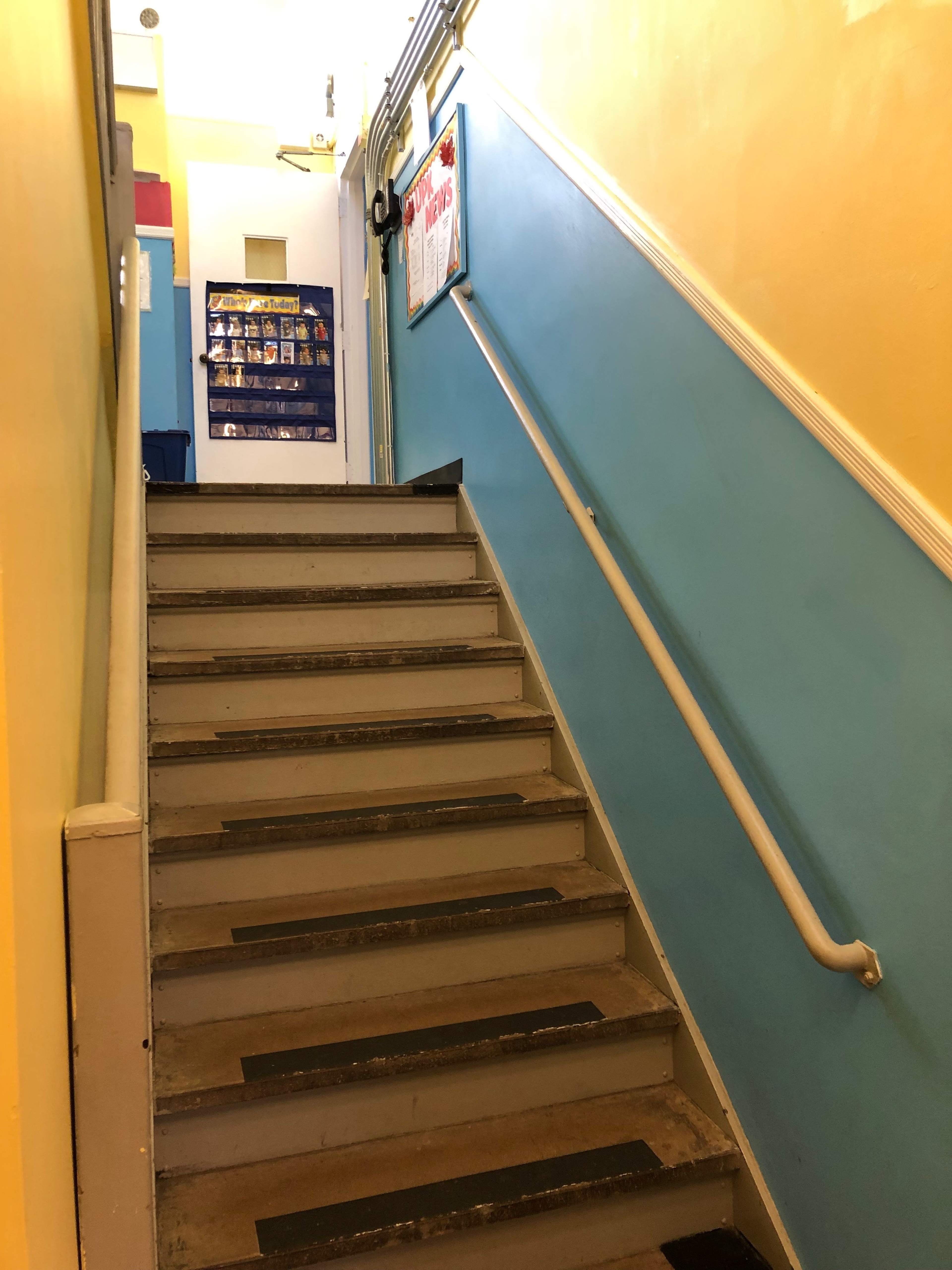 The image shows a staircase leading up, with a blue and yellow walls and a railing on one side.