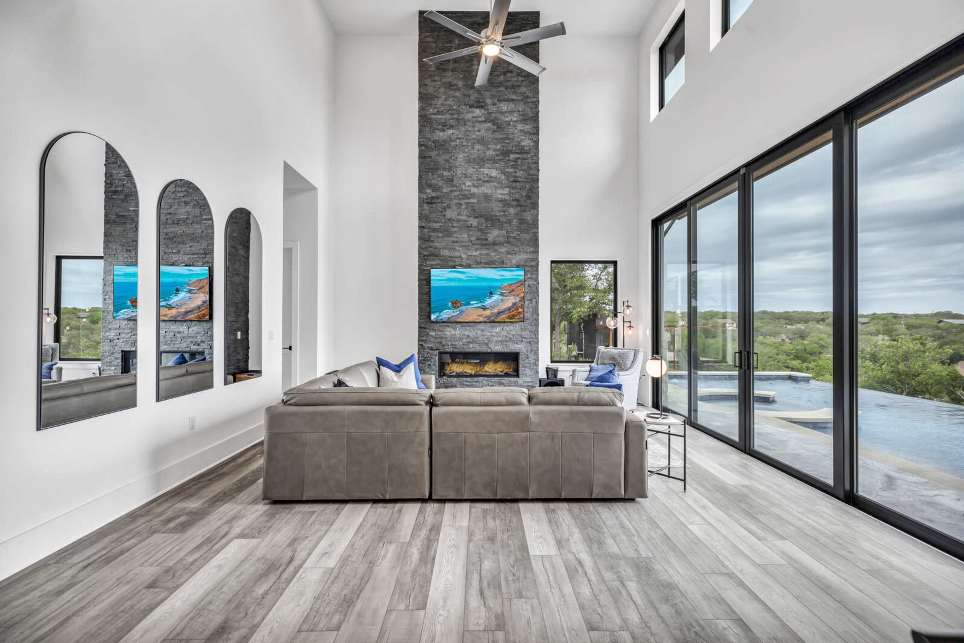 A modern living room features a sectional sofa, a stone fireplace, and large windows overlooking a scenic outdoor view.