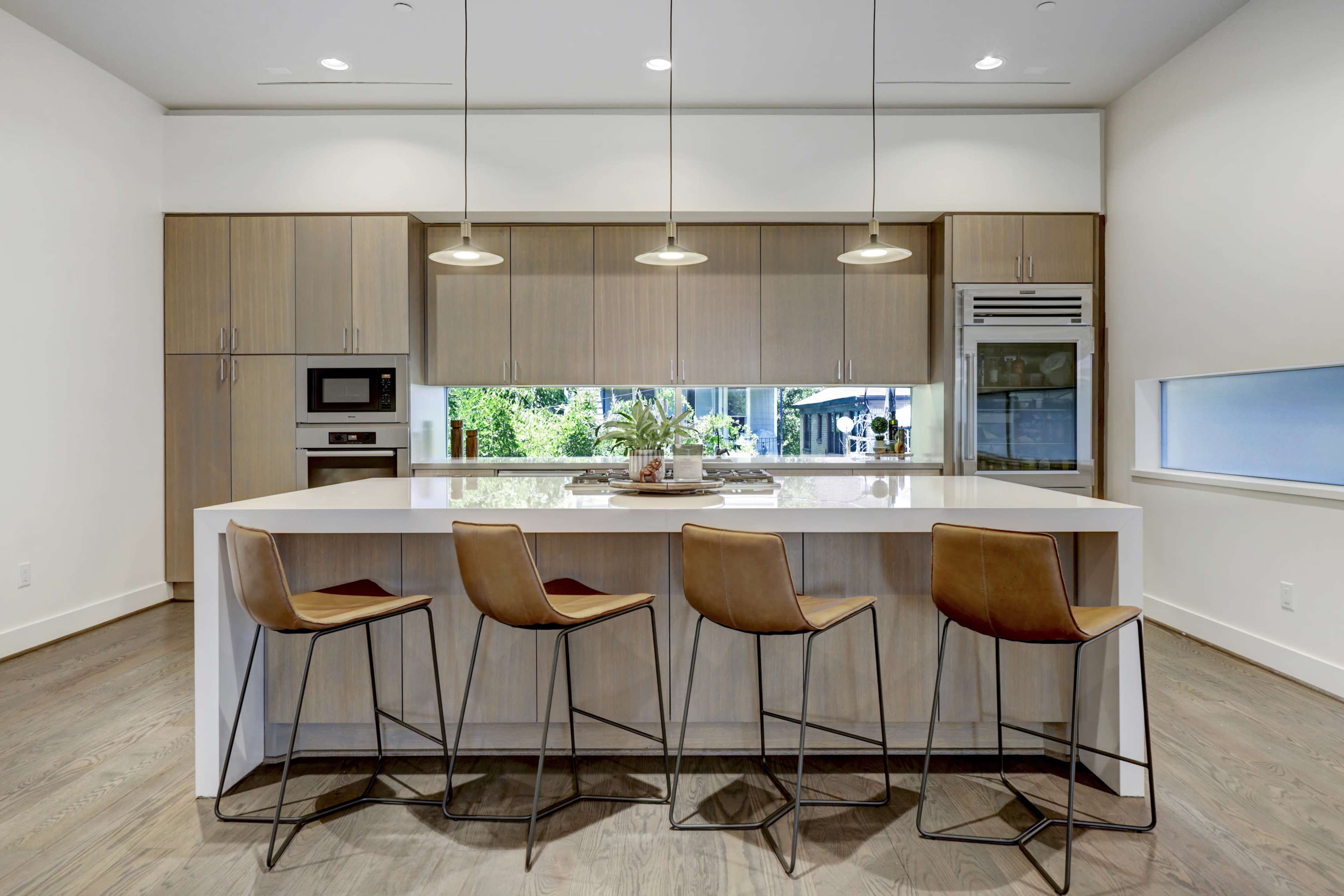 A modern kitchen features a central island with four brown bar stools and stainless steel appliances.
