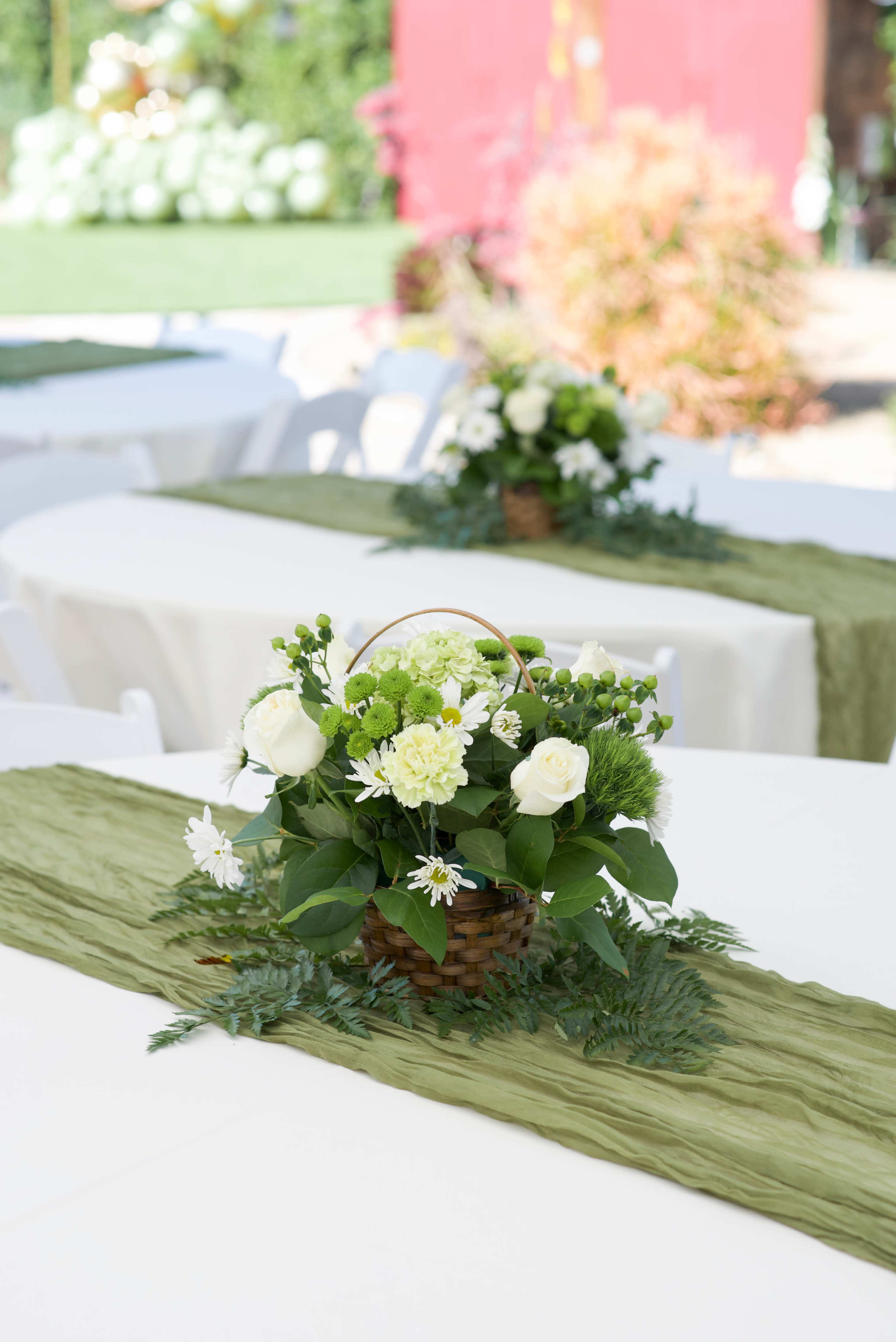 The image shows tables covered with white tablecloths and adorned with green runners, featuring floral arrangements in woven baskets at the center.