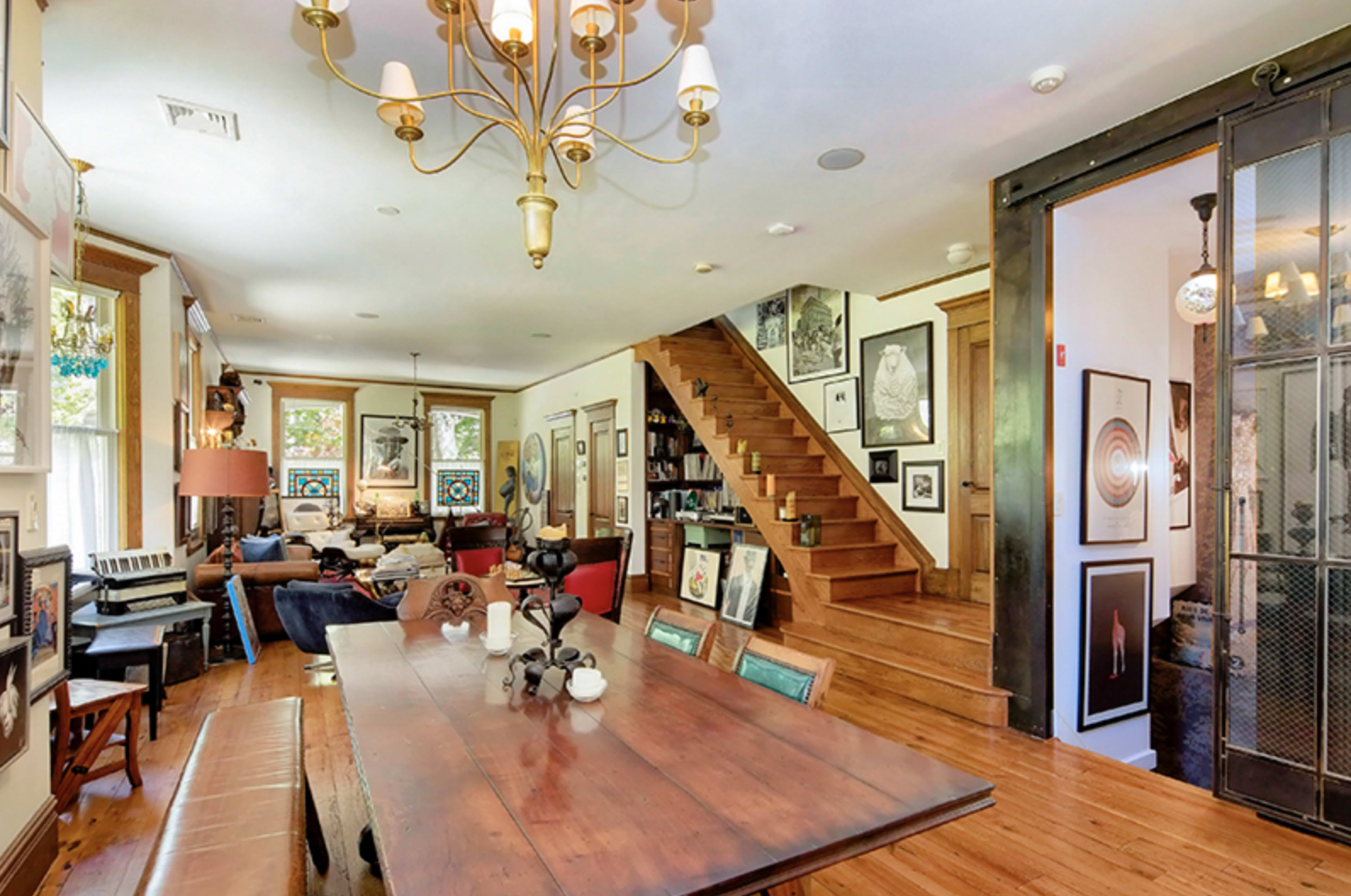 A spacious living area featuring a staircase, a large dining table, and walls adorned with various framed artworks.