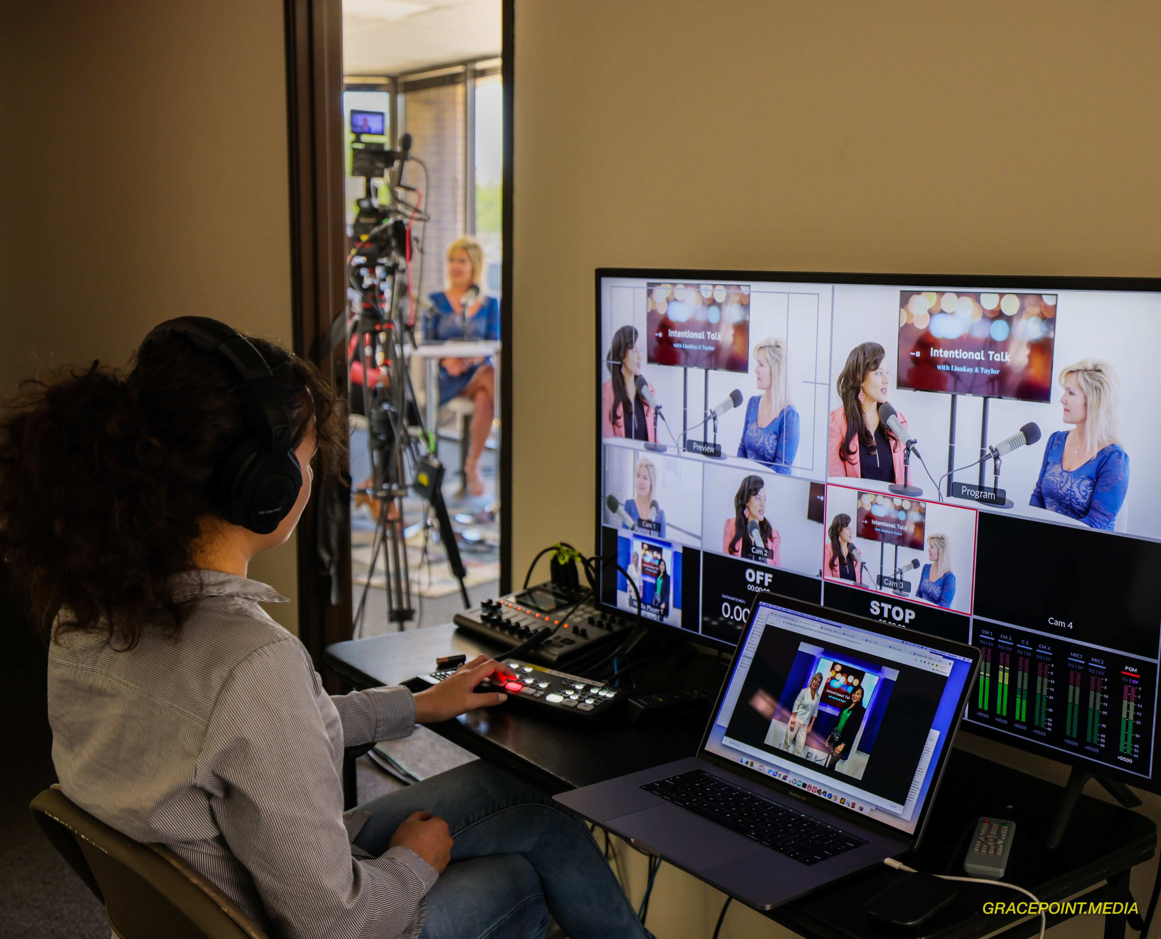 A woman operates a video production setup while monitoring multiple camera feeds on a screen.
