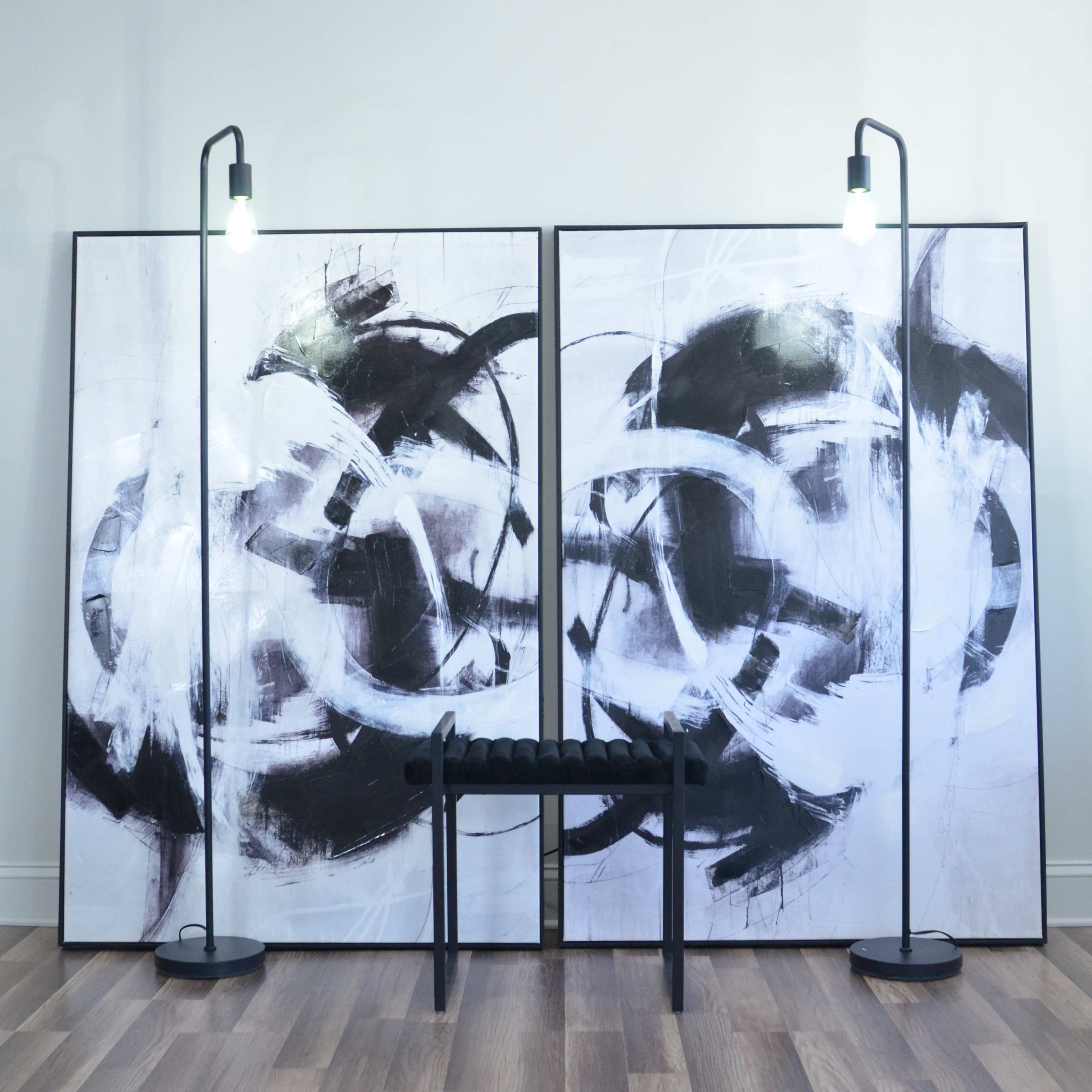 The image features a minimalist interior with two large abstract black-and-white paintings flanking a bench, illuminated by two standing lamps.
