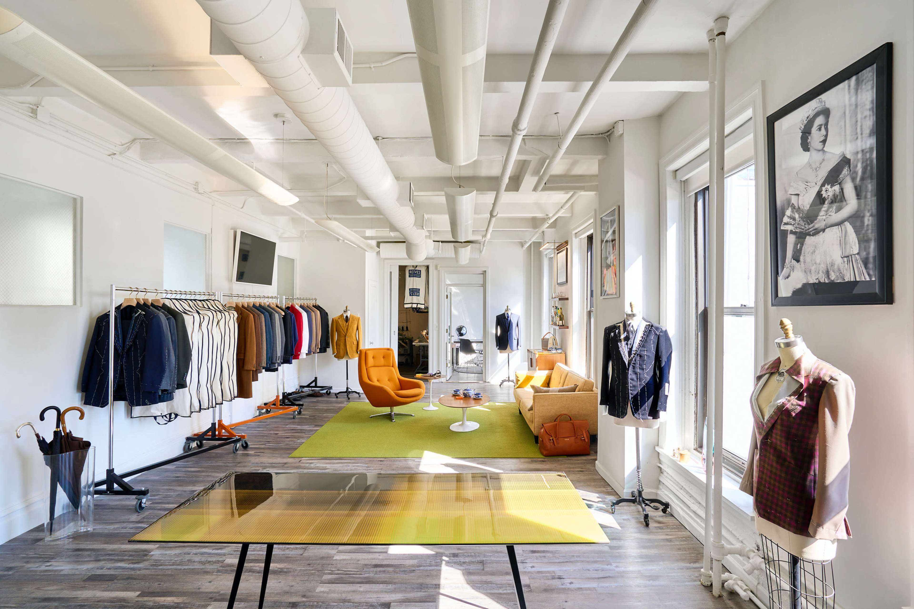 A bright, modern clothing store features a variety of garments displayed on racks, an orange chair, and large windows letting in natural light.