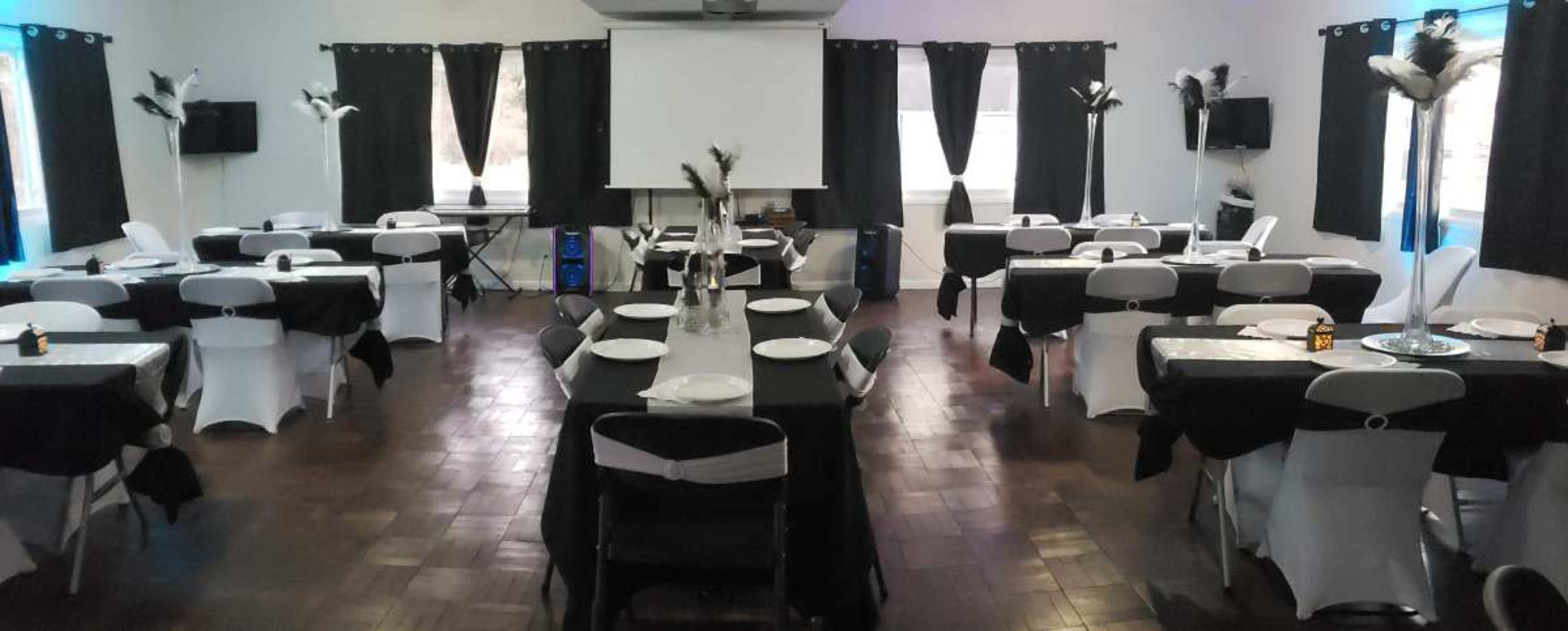 A banquet hall is set up with multiple tables covered in black and white linens, accented by centerpieces and black curtains.
