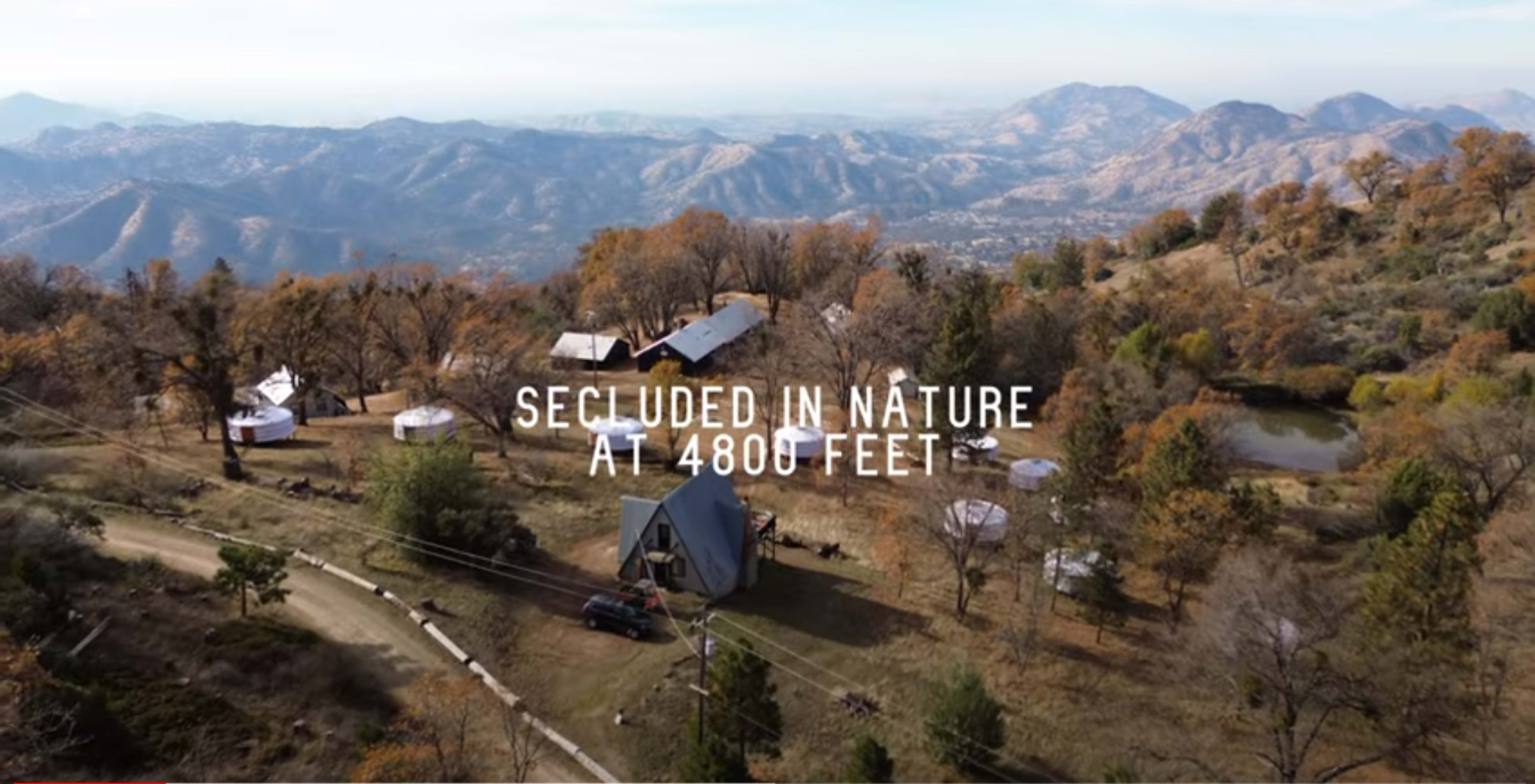 Aerial view of a remote camping site at 4,800 feet elevation, featuring tents and a cabin surrounded by hills and trees.