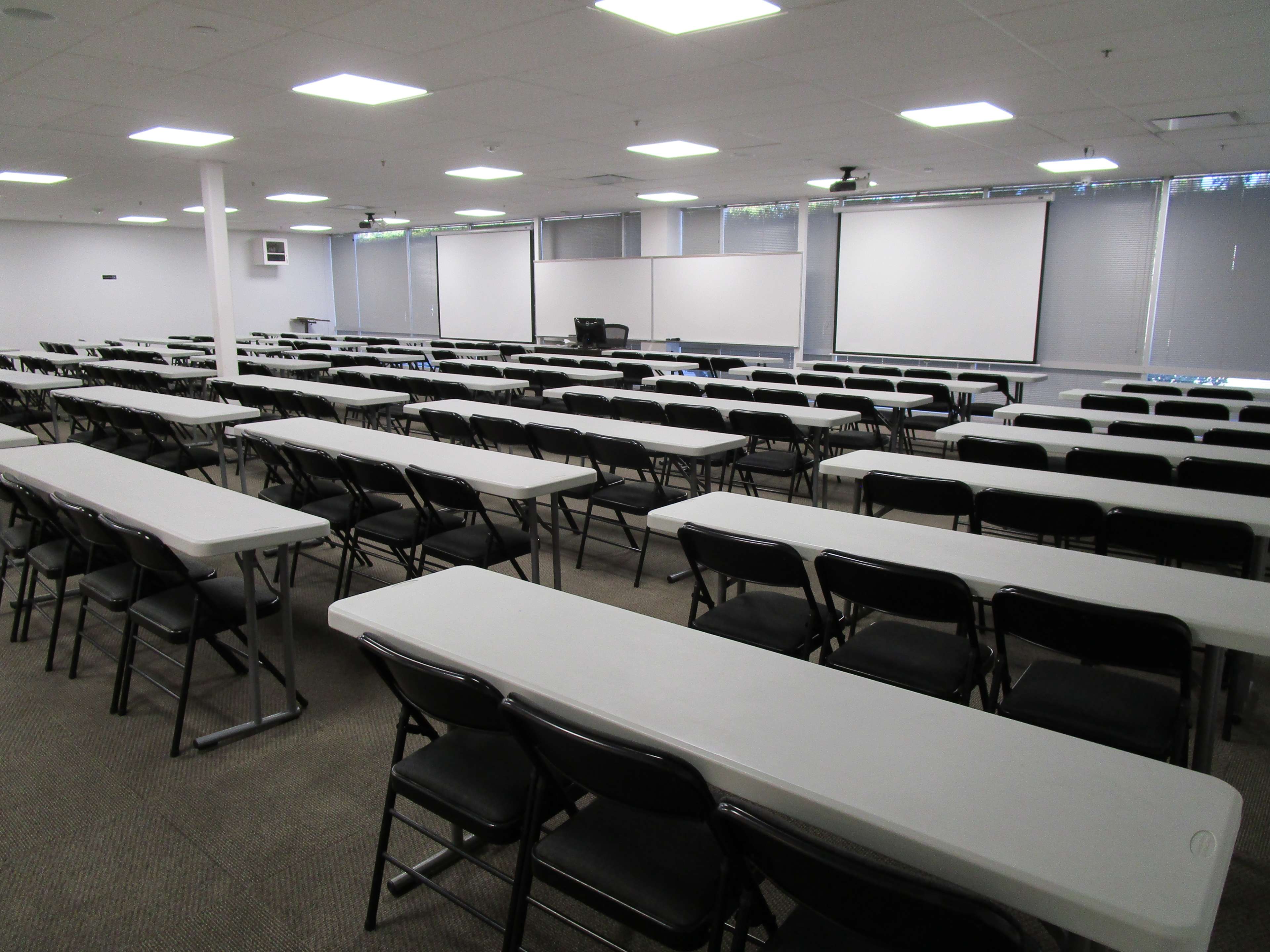 A large, empty classroom with rows of tables and chairs arranged for a meeting or training session.