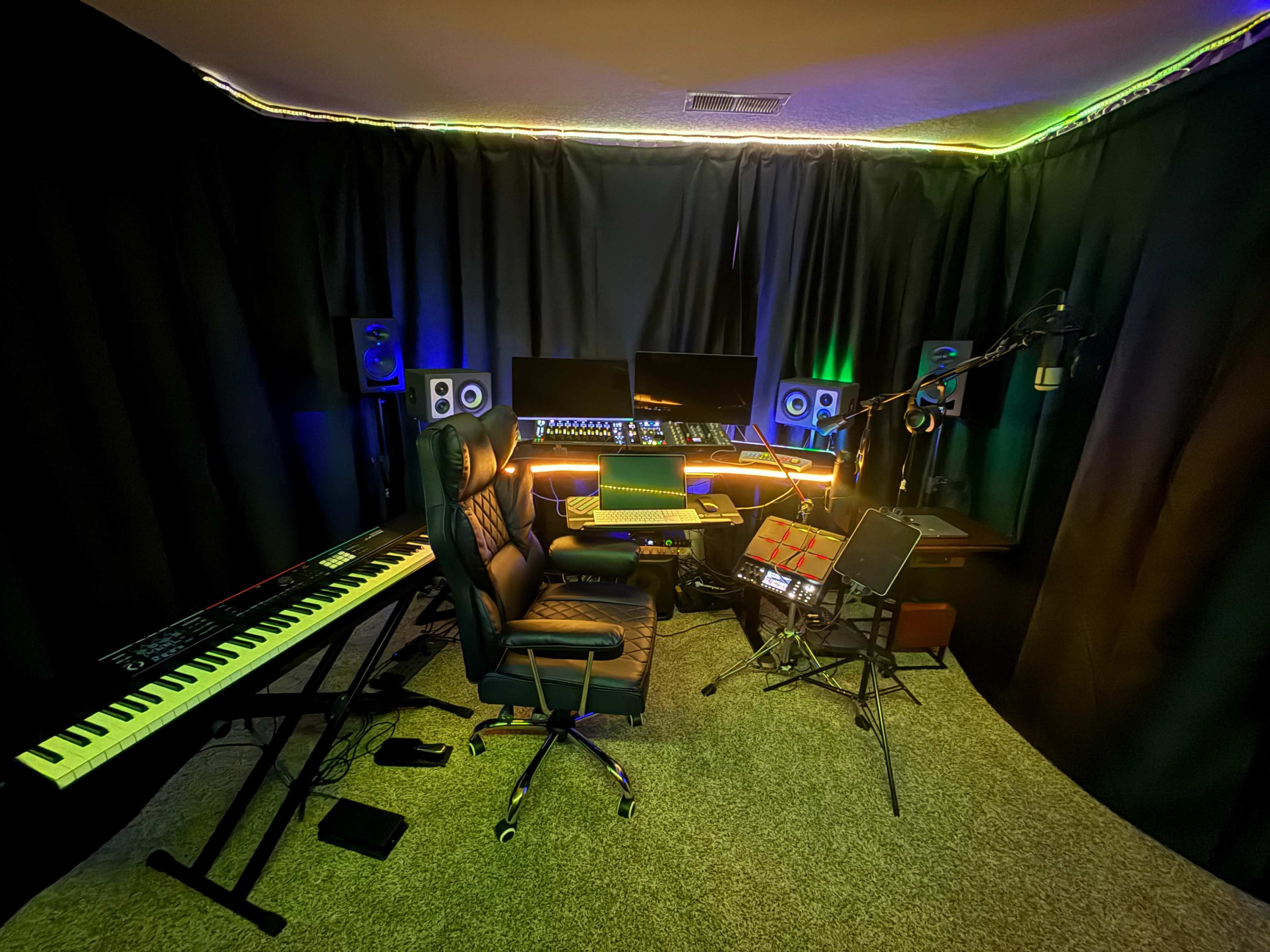 The image shows a music production studio with a keyboard, a chair, multiple monitors, speakers, and a microphone, all set against a dark backdrop.