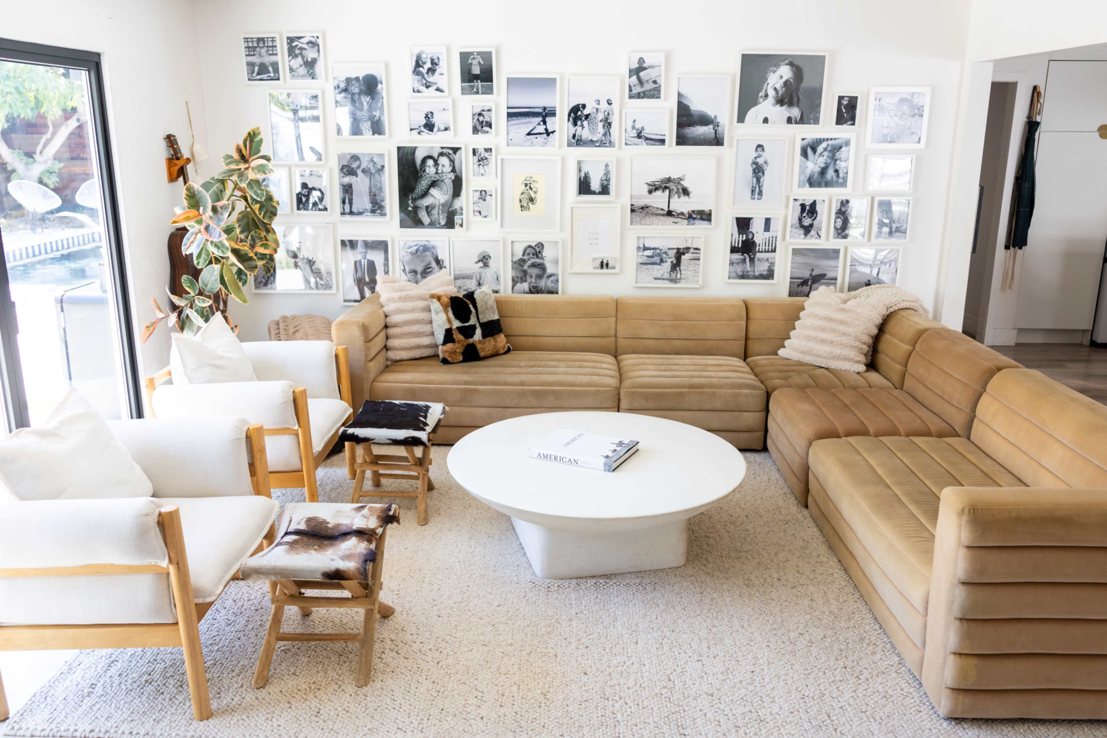The image shows a modern living room with a large brown sectional sofa, white accent chairs, a round coffee table, and a wall decorated with black-and-white photographs.