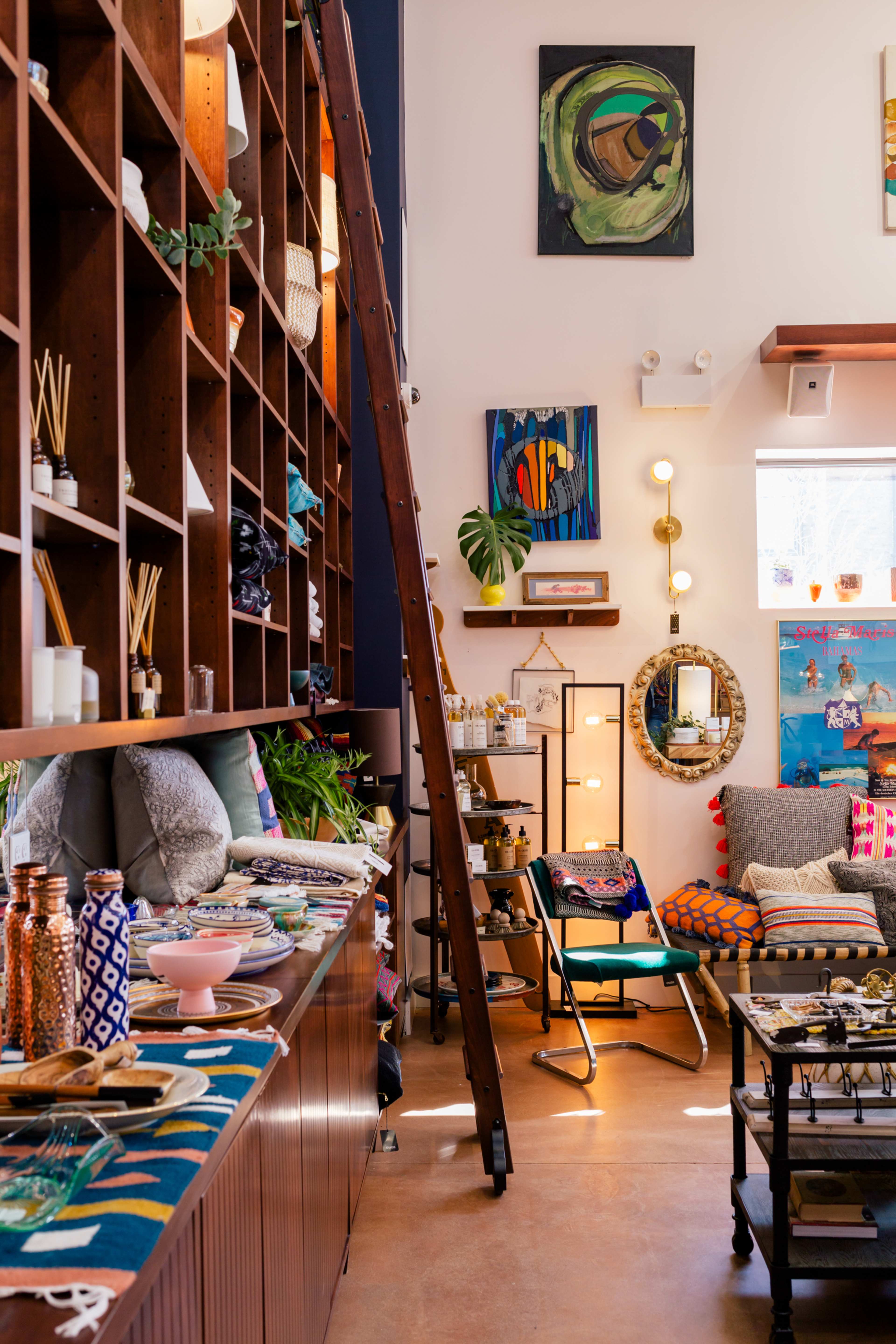 A cozy interior of a shop featuring wooden shelves lined with various decorative items, artwork on the walls, and a ladder positioned against the shelves.