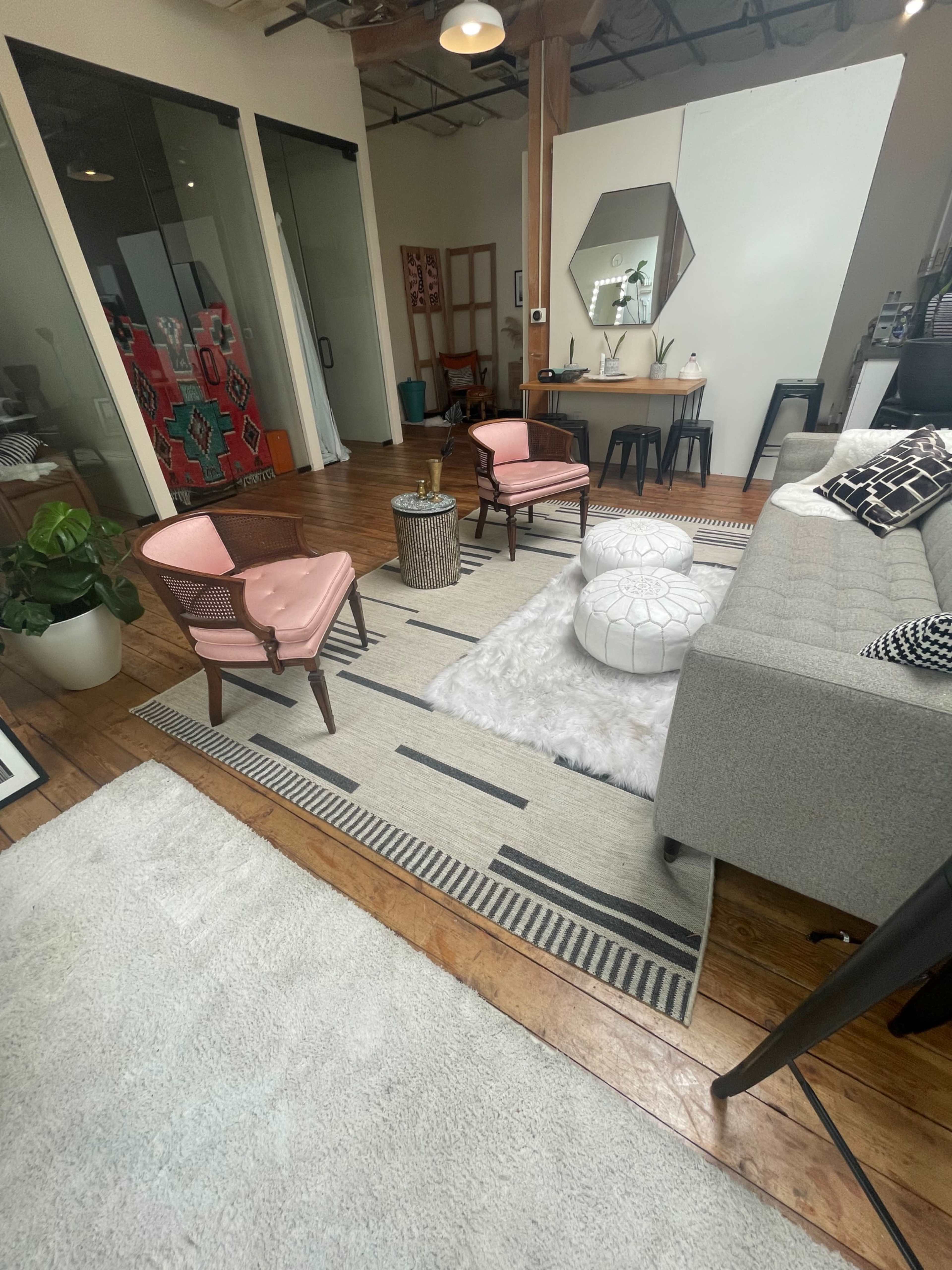 A modern living space featuring a gray sofa, two pink armchairs, a round coffee table on a patterned rug, and a white faux fur throw on the floor.