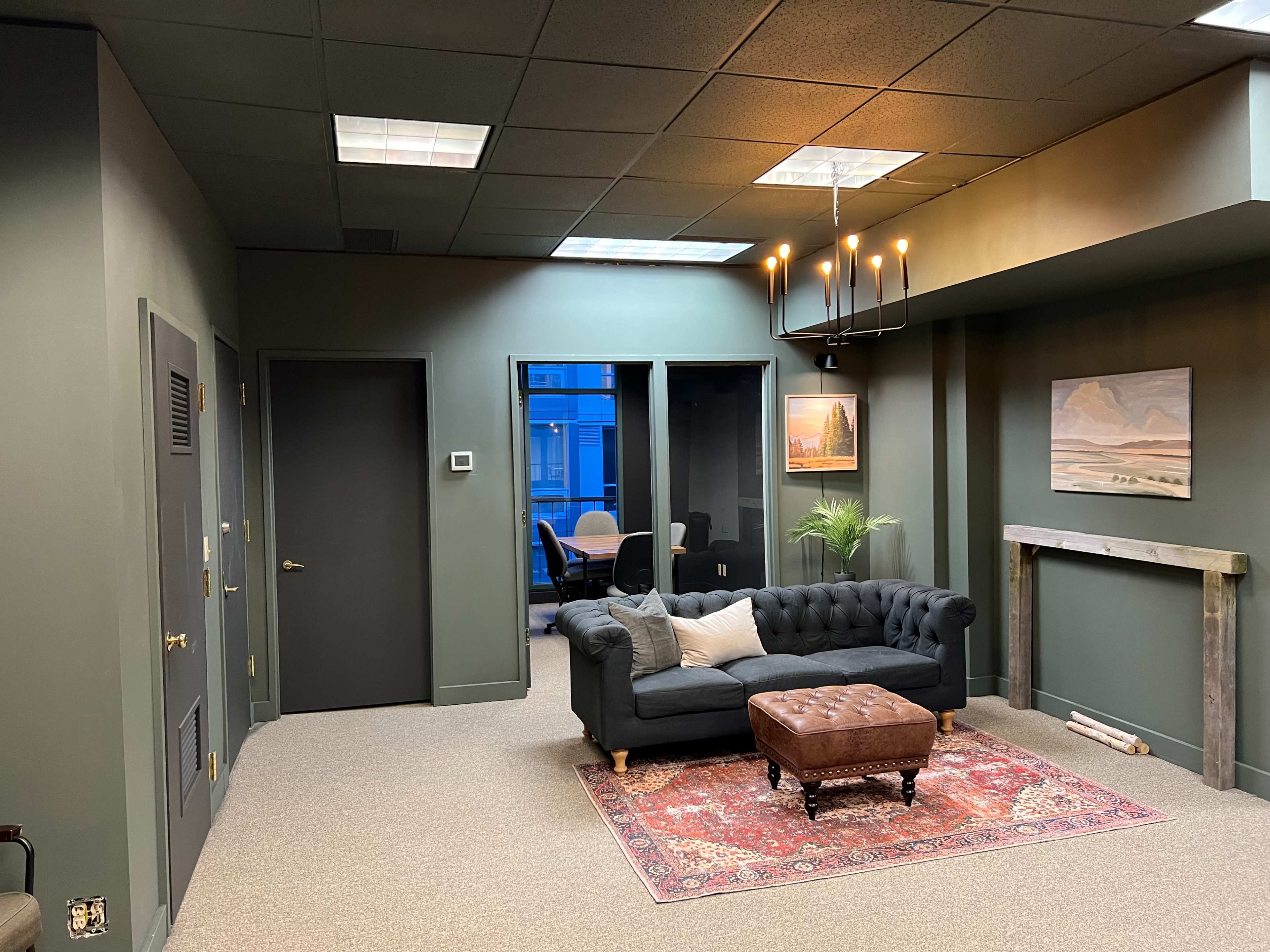A modern office waiting area with a dark green color scheme, featuring a tufted sofa, a coffee table, and a framed painting on the wall.