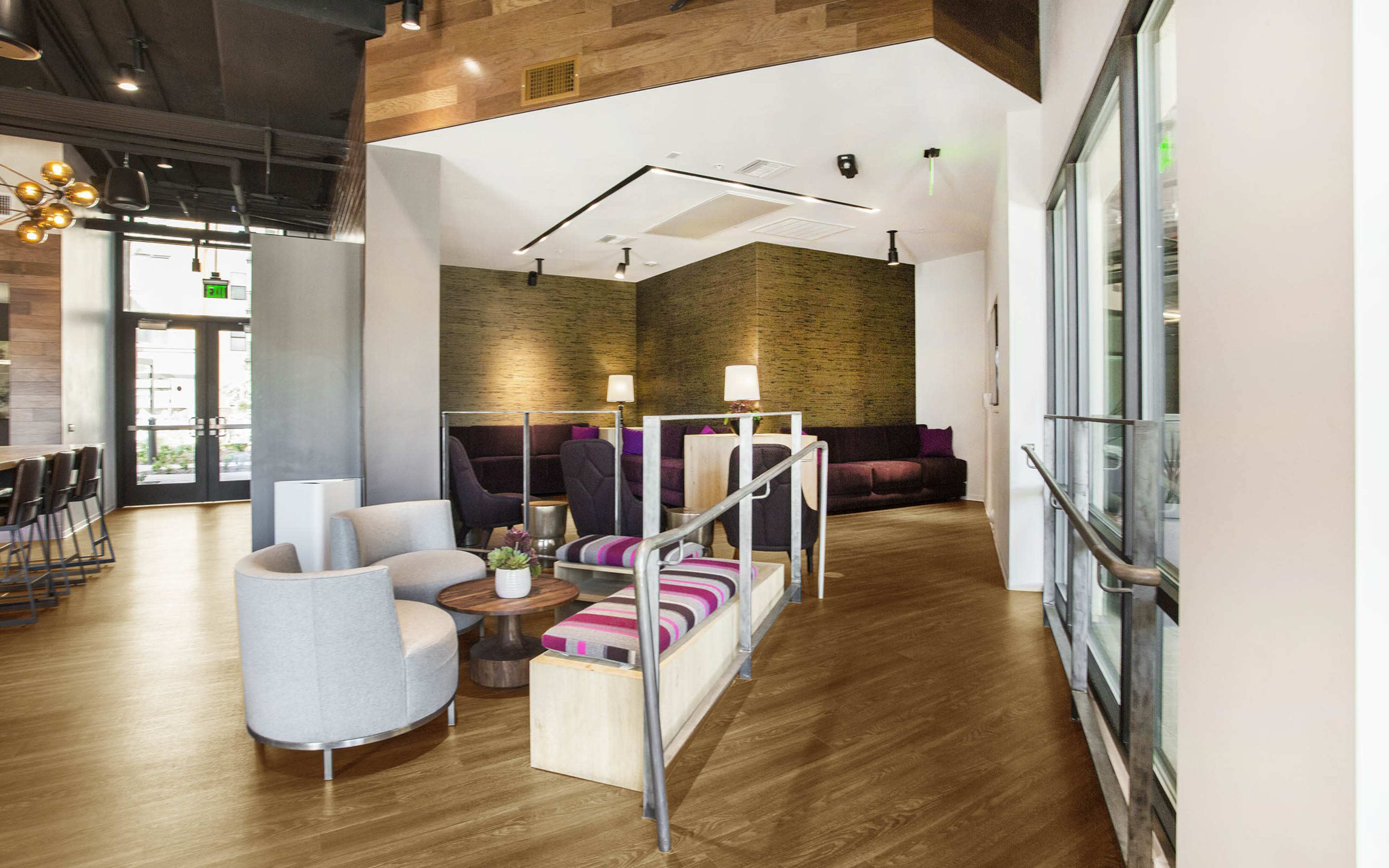 A modern interior space featuring a seating area with gray chairs and a wooden floor, alongside a bar counter and decorative lighting.