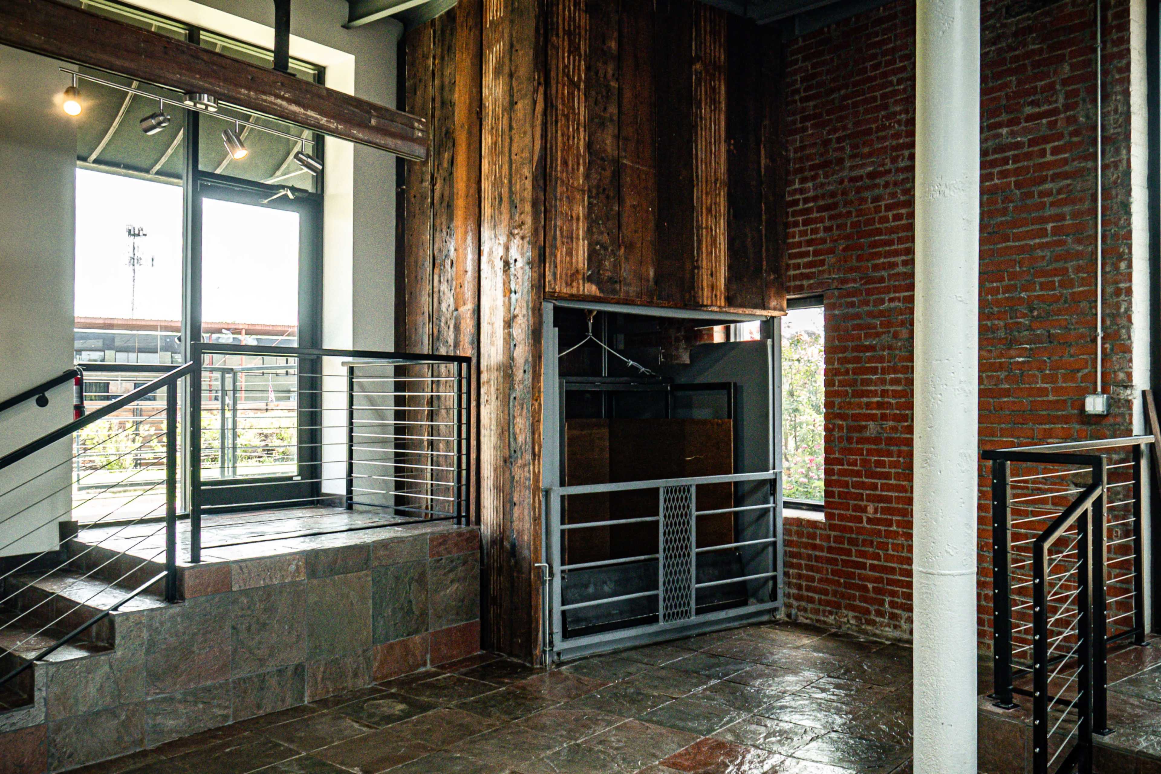The image shows an industrial-style interior featuring a combination of exposed brick walls, wooden beams, and a staircase with metal railings.