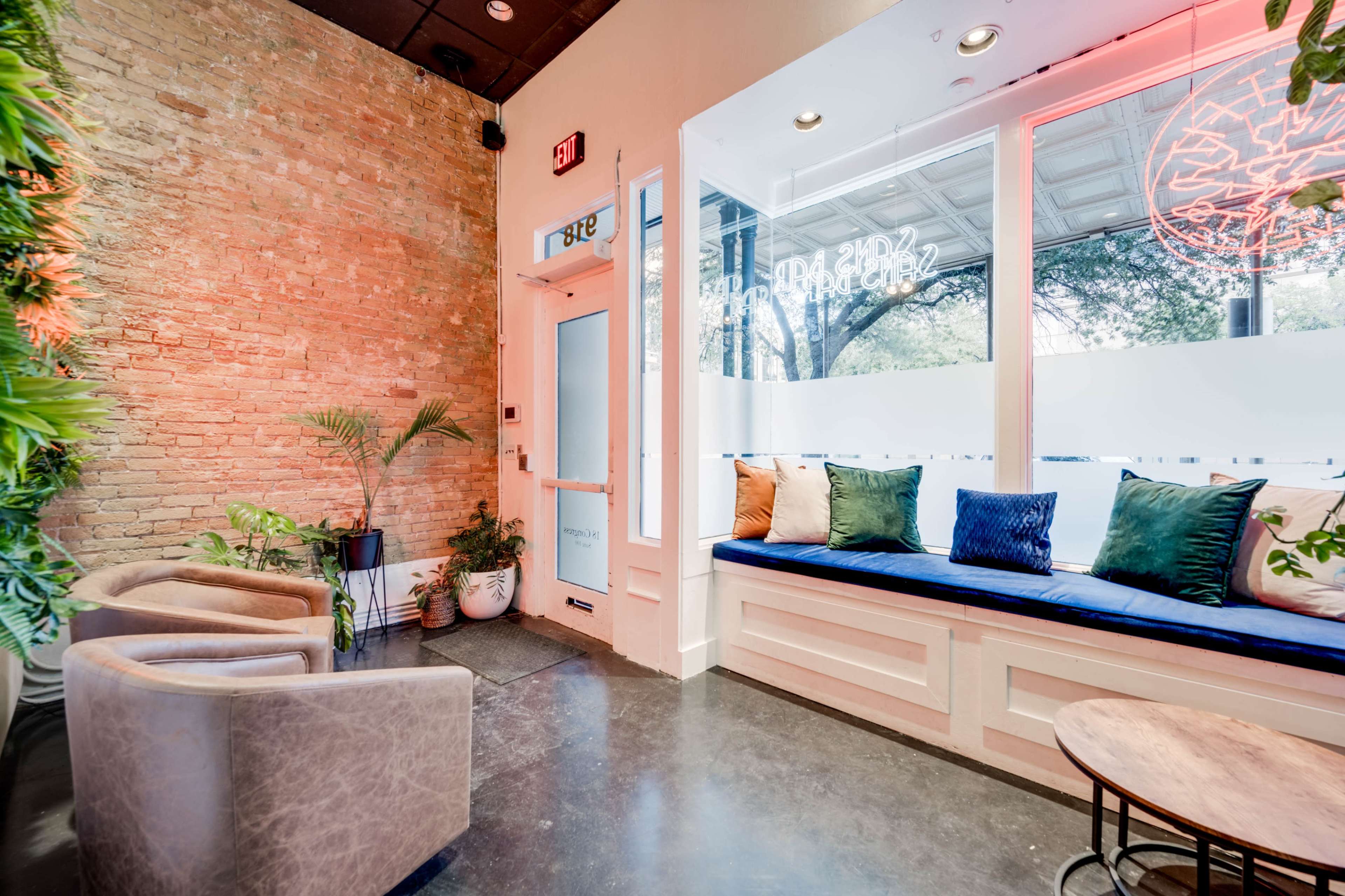 The image shows a modern interior with a cozy seating area featuring a window bench with cushions, plants, and a small table.
