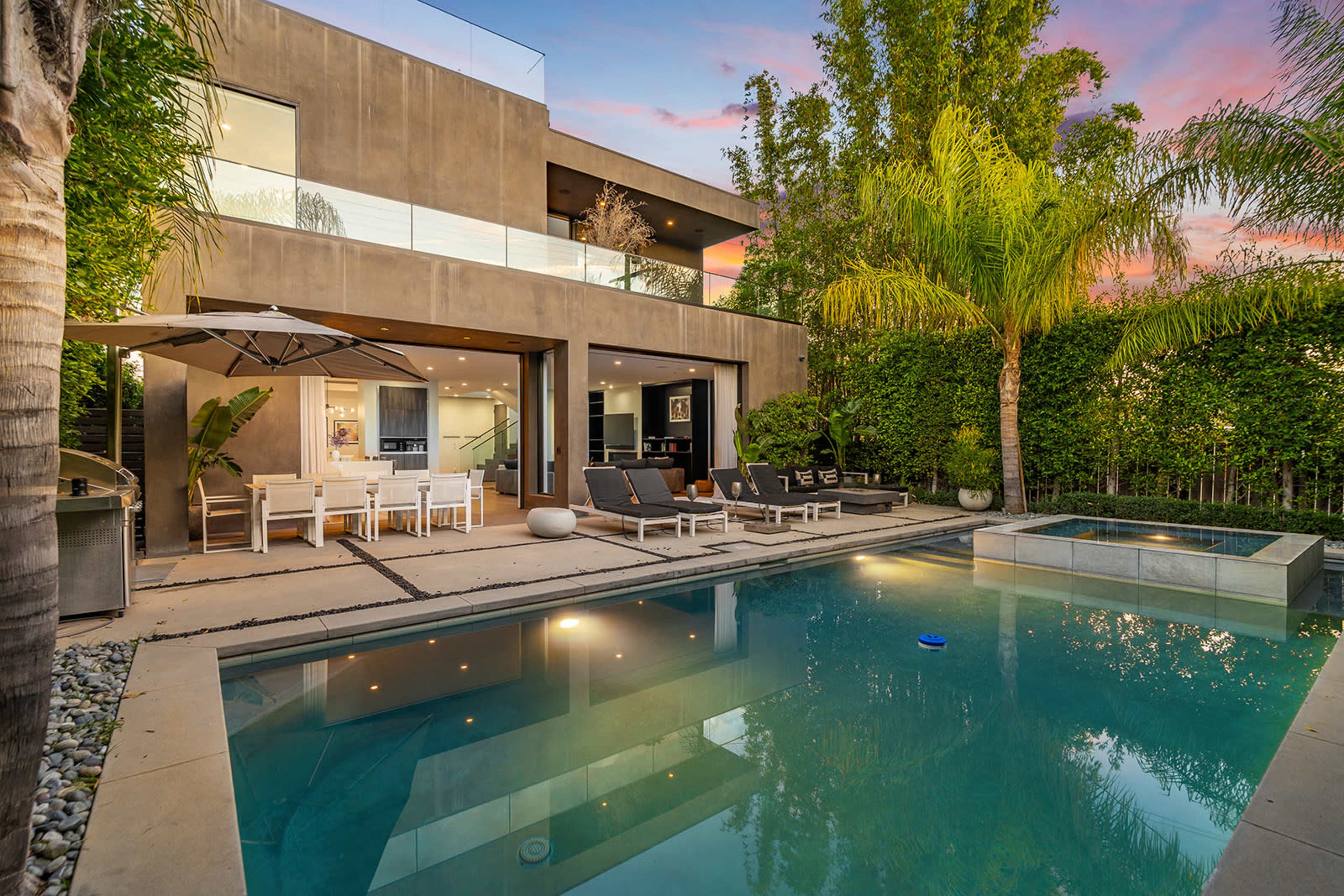 A modern two-story house with a swimming pool, outdoor seating area, and landscaped greenery in the backyard.