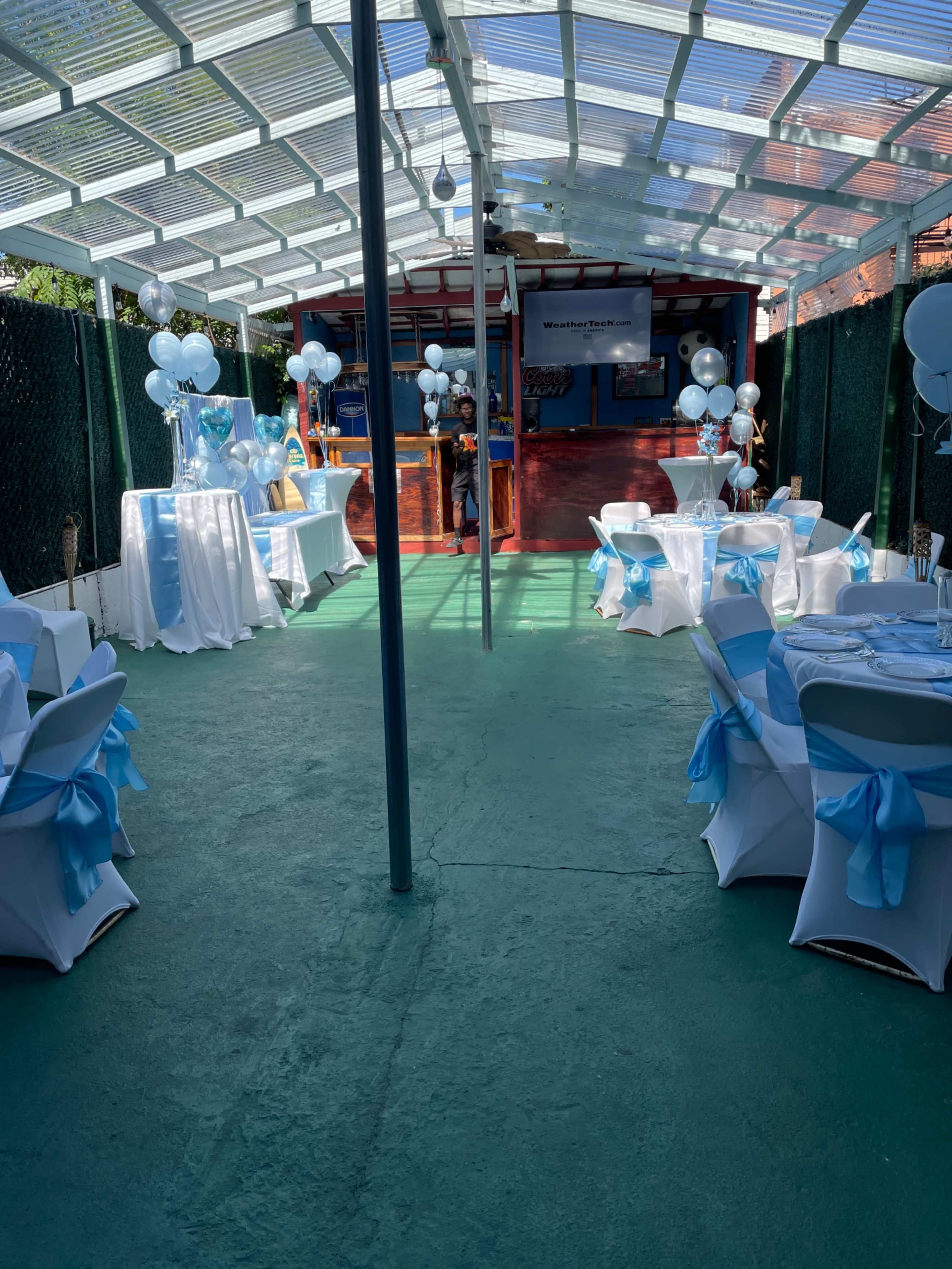 A decorated outdoor space with tables set up for a celebration, featuring blue and white balloons and table linens.