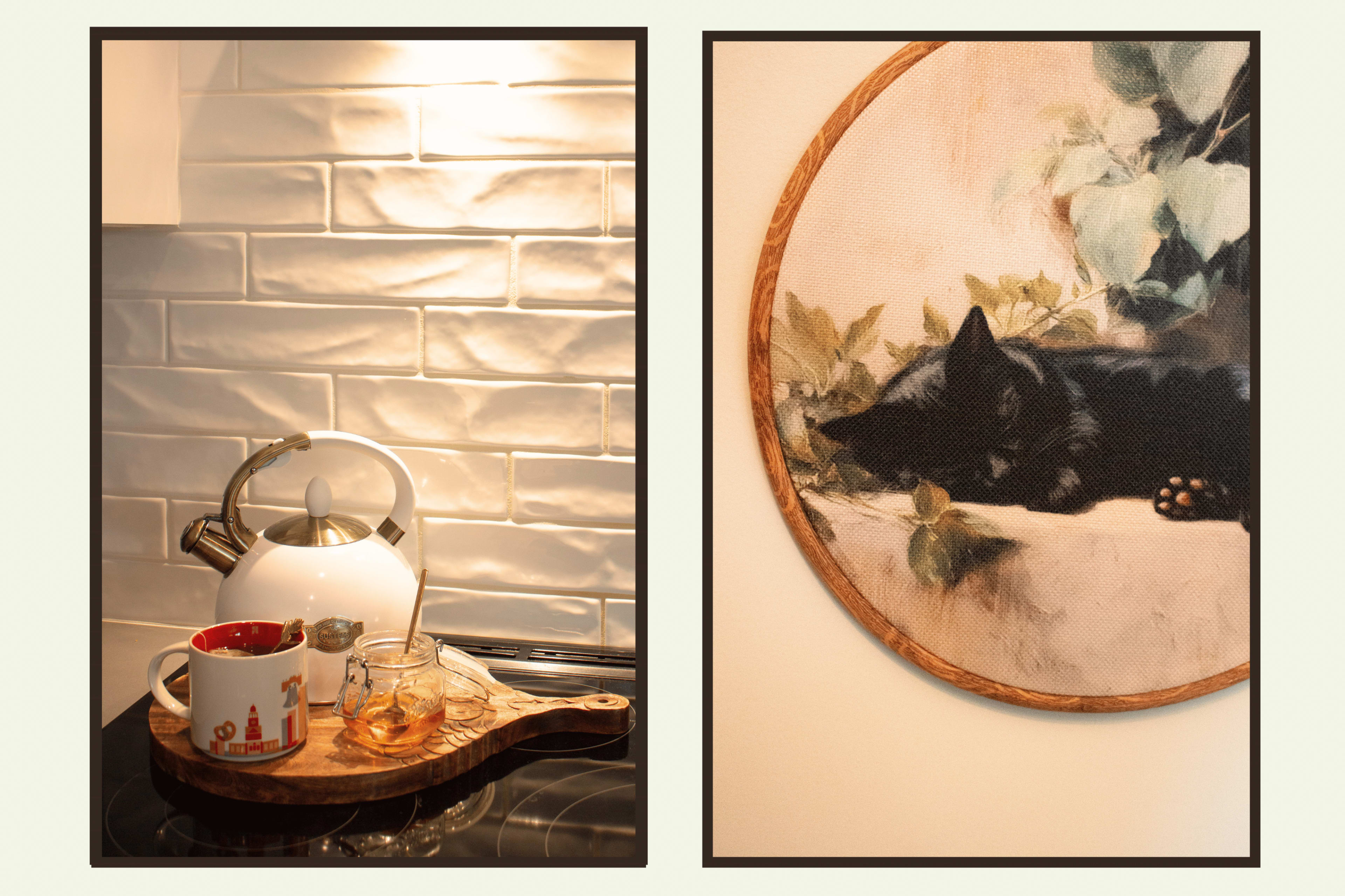 A white kettle and a wooden tray with a mug and glass are set on a stovetop beside a wall with textured tiles, while a round artwork depicting a sleeping black cat is mounted on another wall.
