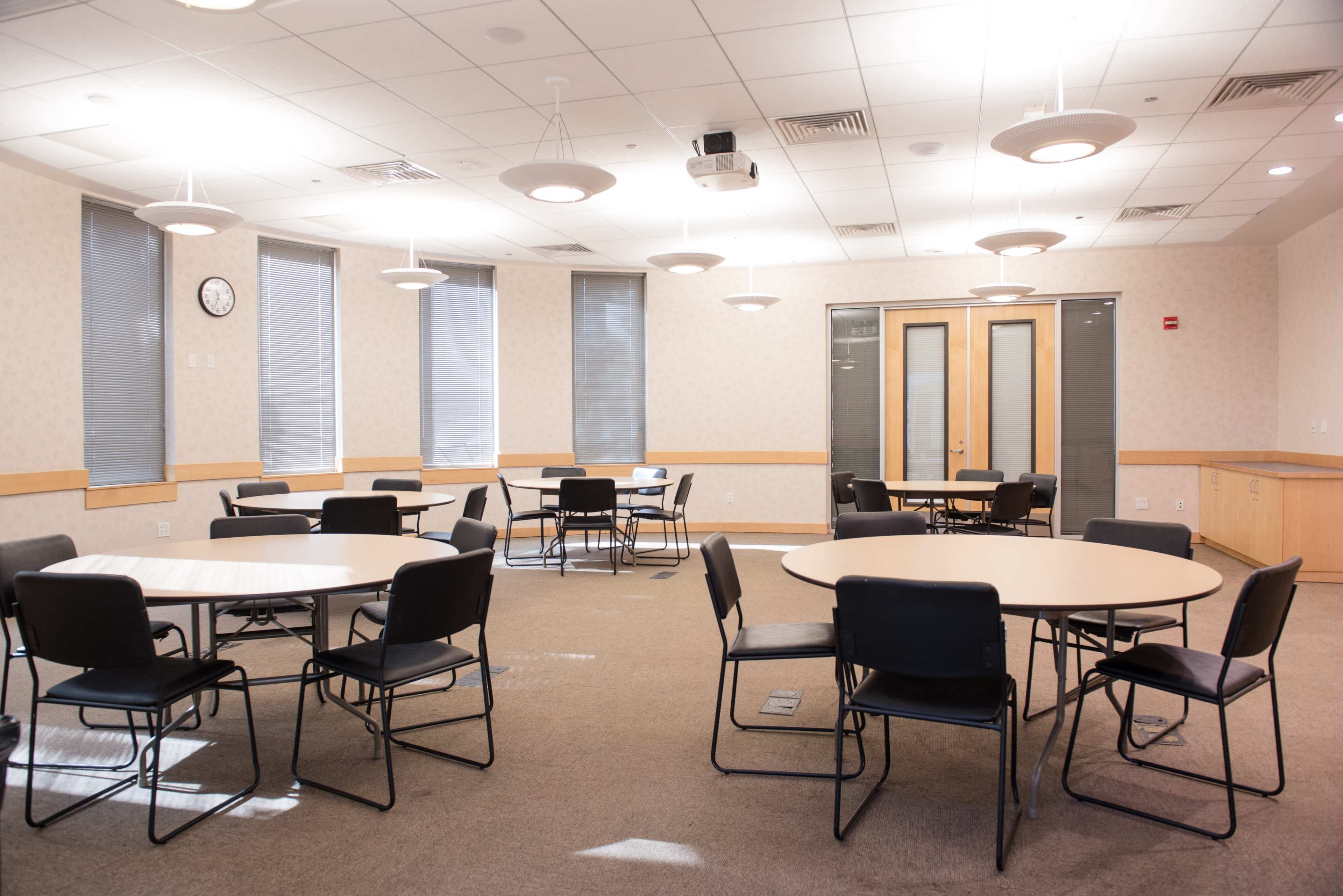 A well-lit meeting room with several round tables and chairs arranged throughout the space.