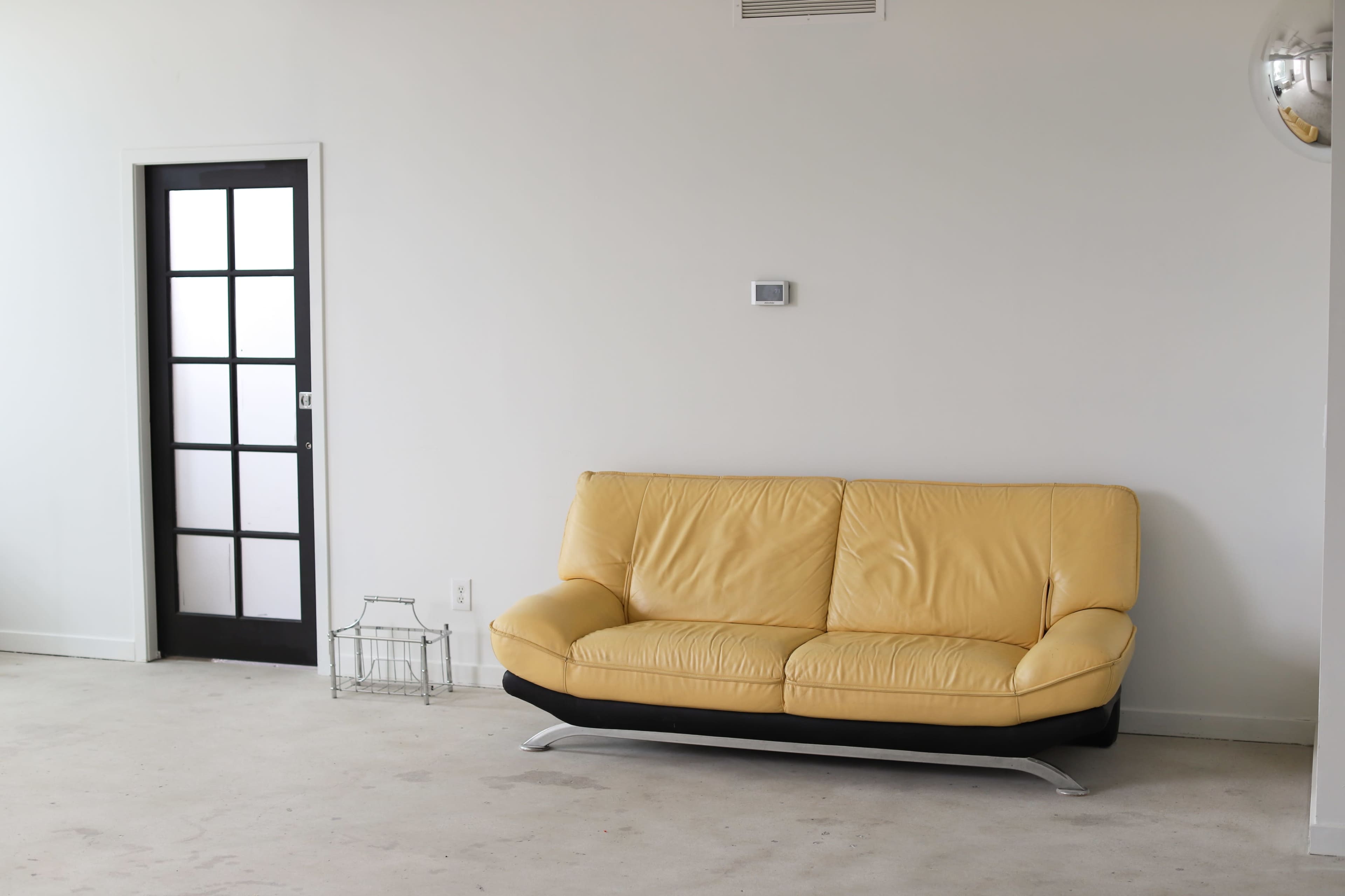 A yellow leather sofa is positioned against a plain wall, next to a door with a grid-patterned glass panel.
