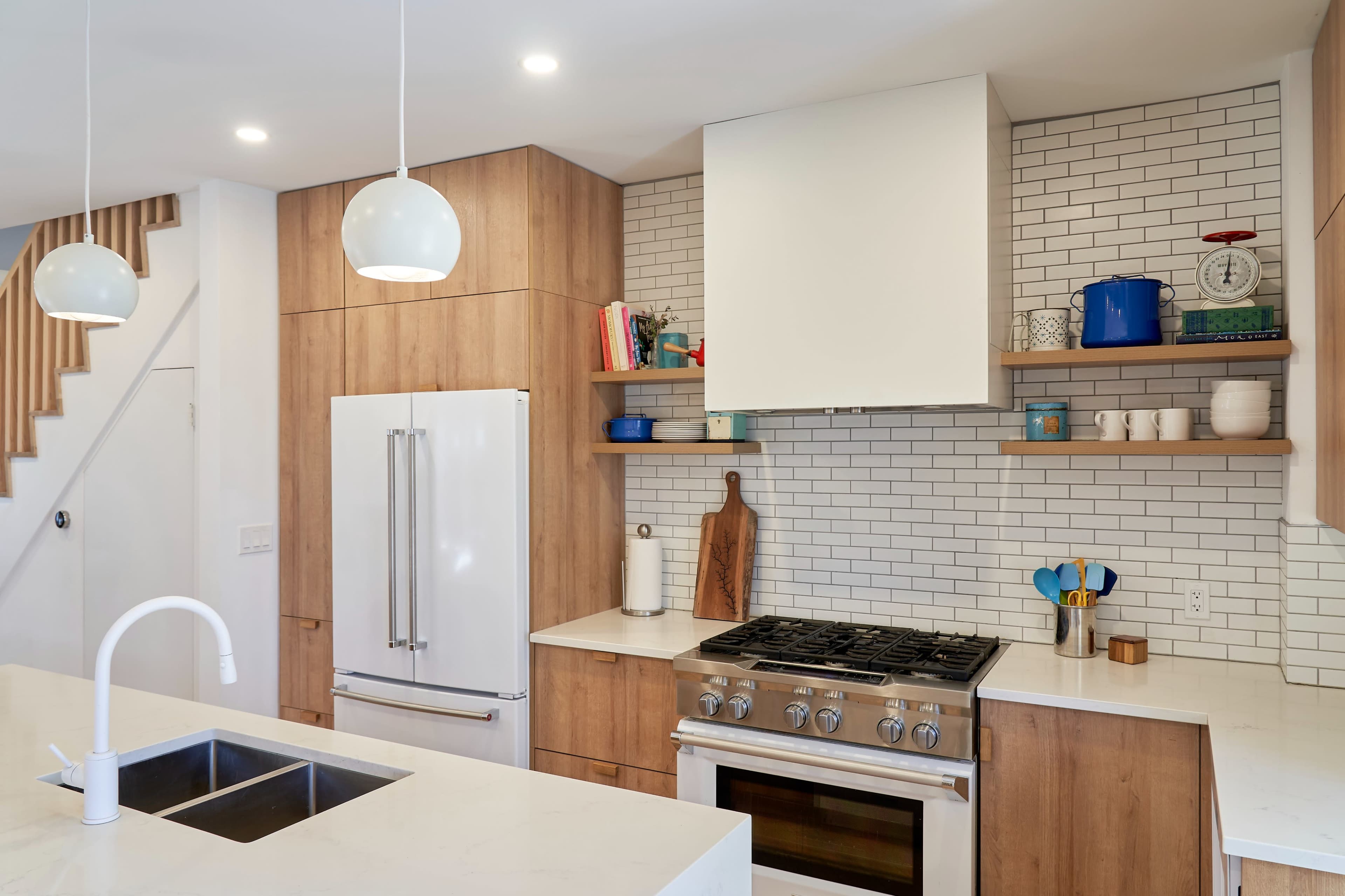 A modern kitchen with wood cabinetry, a stainless steel refrigerator, a gas stove, and white subway tile backsplash.