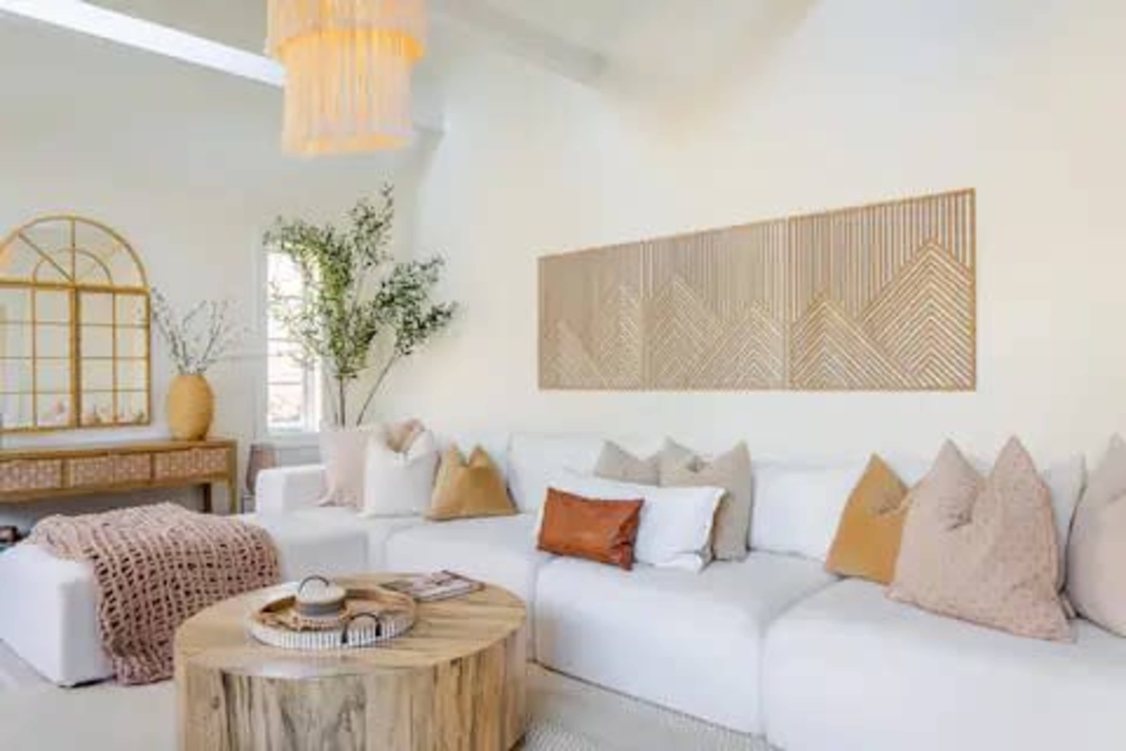 The image shows a modern living room with a large white sectional sofa, a wooden coffee table, and a wall decoration featuring geometric patterns.
