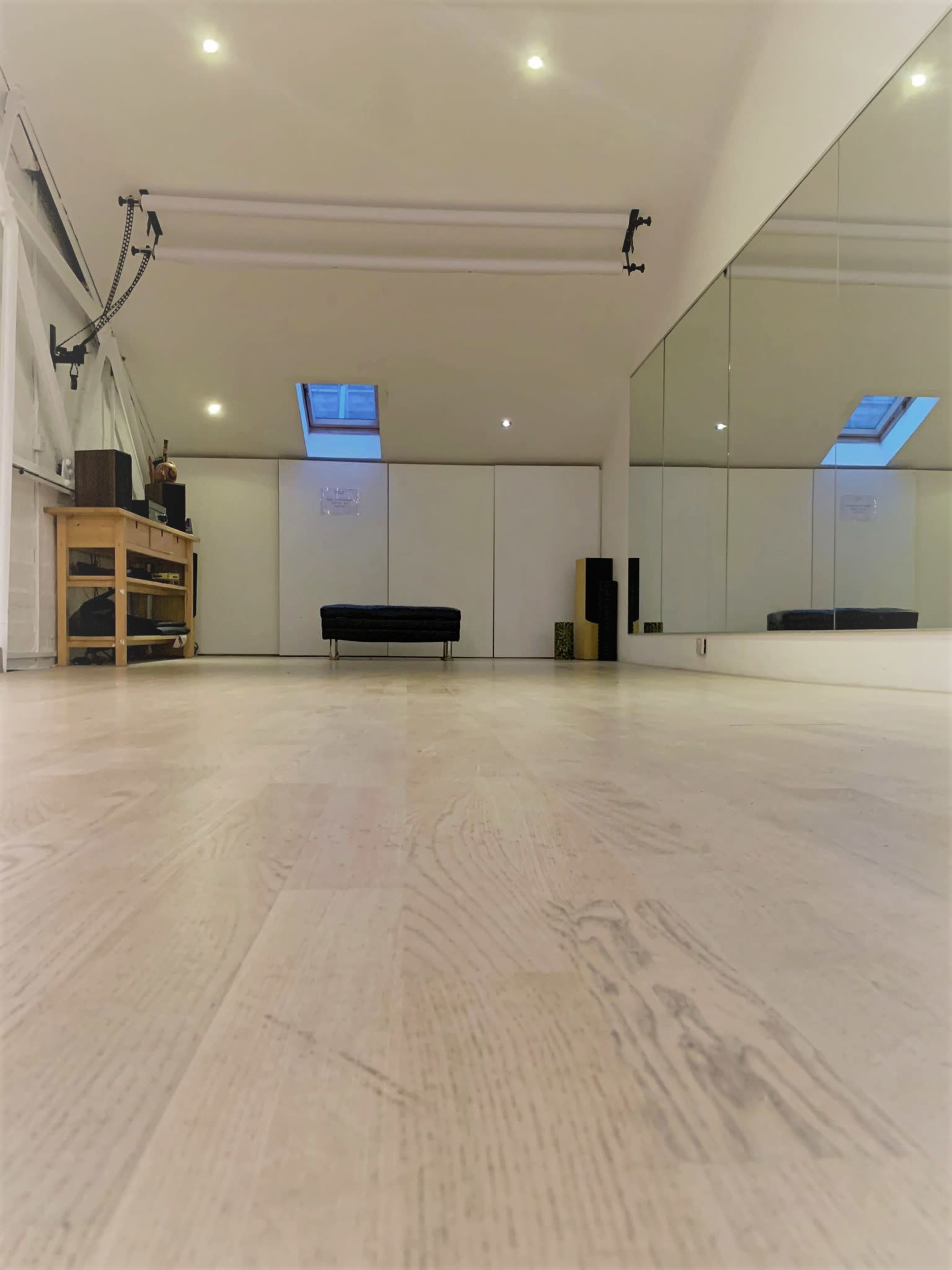 A spacious room features wooden flooring, large mirrors on one wall, and a skylight above.