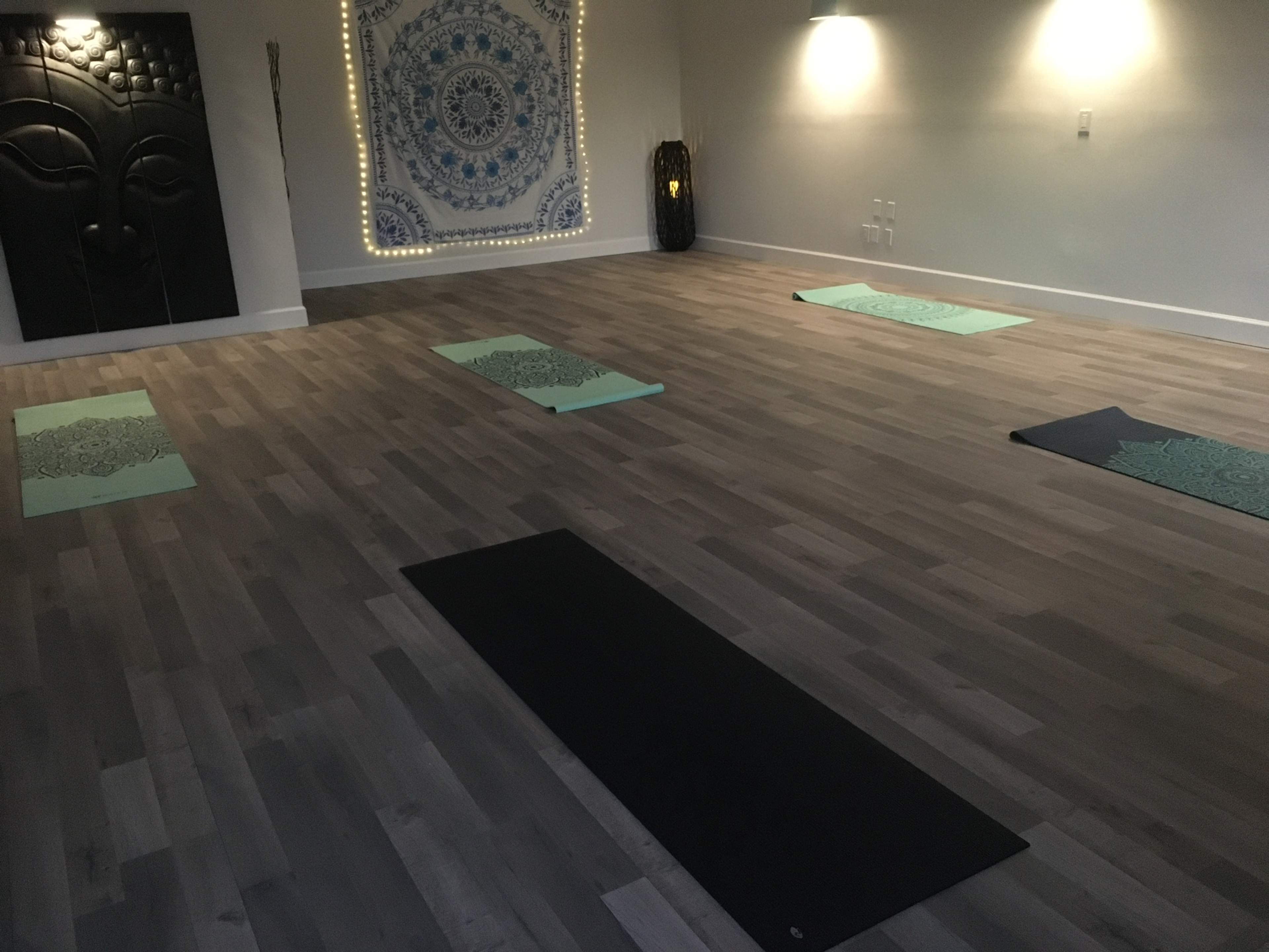A yoga studio with several exercise mats arranged on a wooden floor, illuminated by soft lighting and decorated with a large wall tapestry.