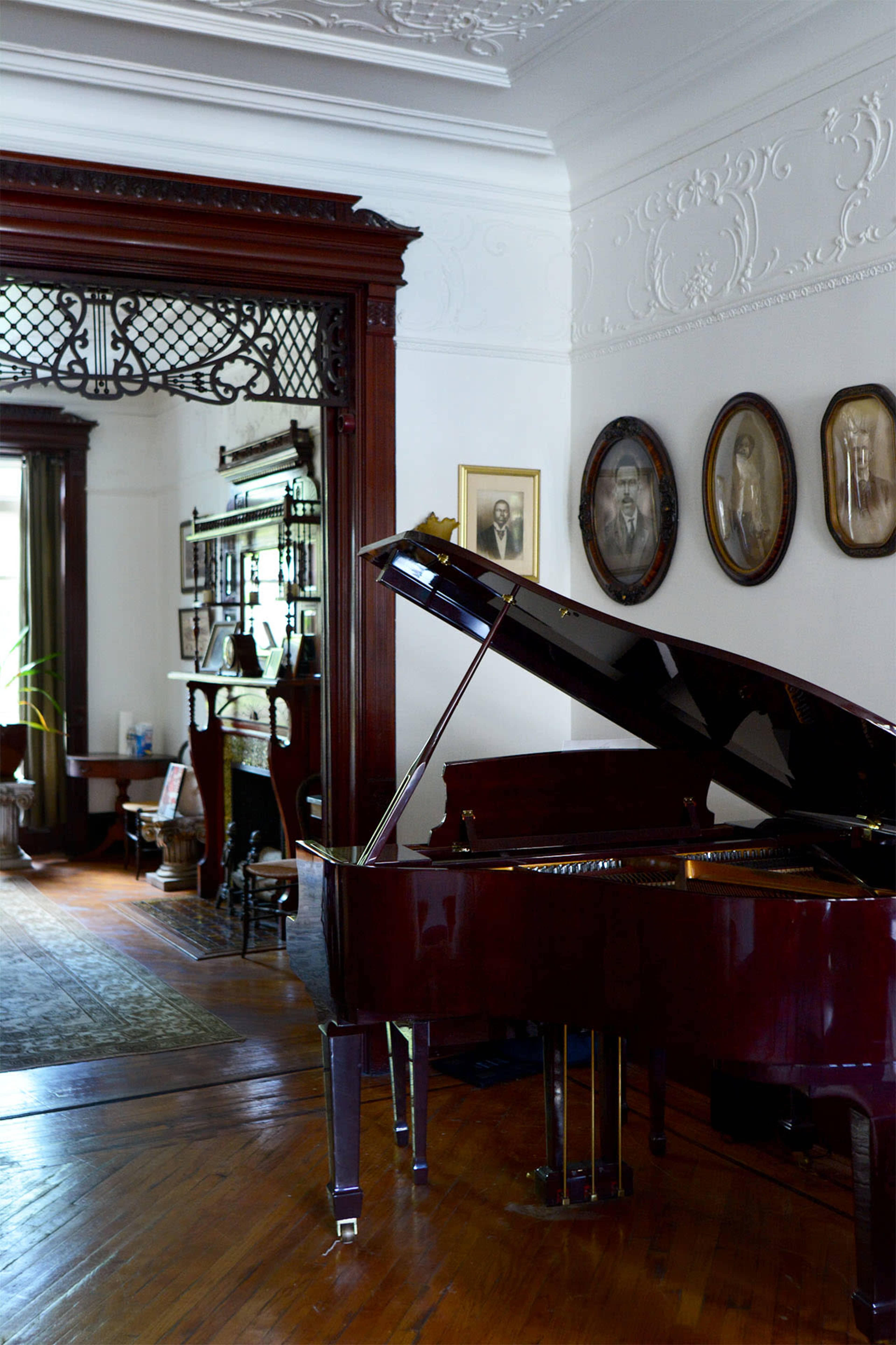 A grand piano sits in the foreground of an elegant room adorned with vintage decor and framed portraits on the walls.