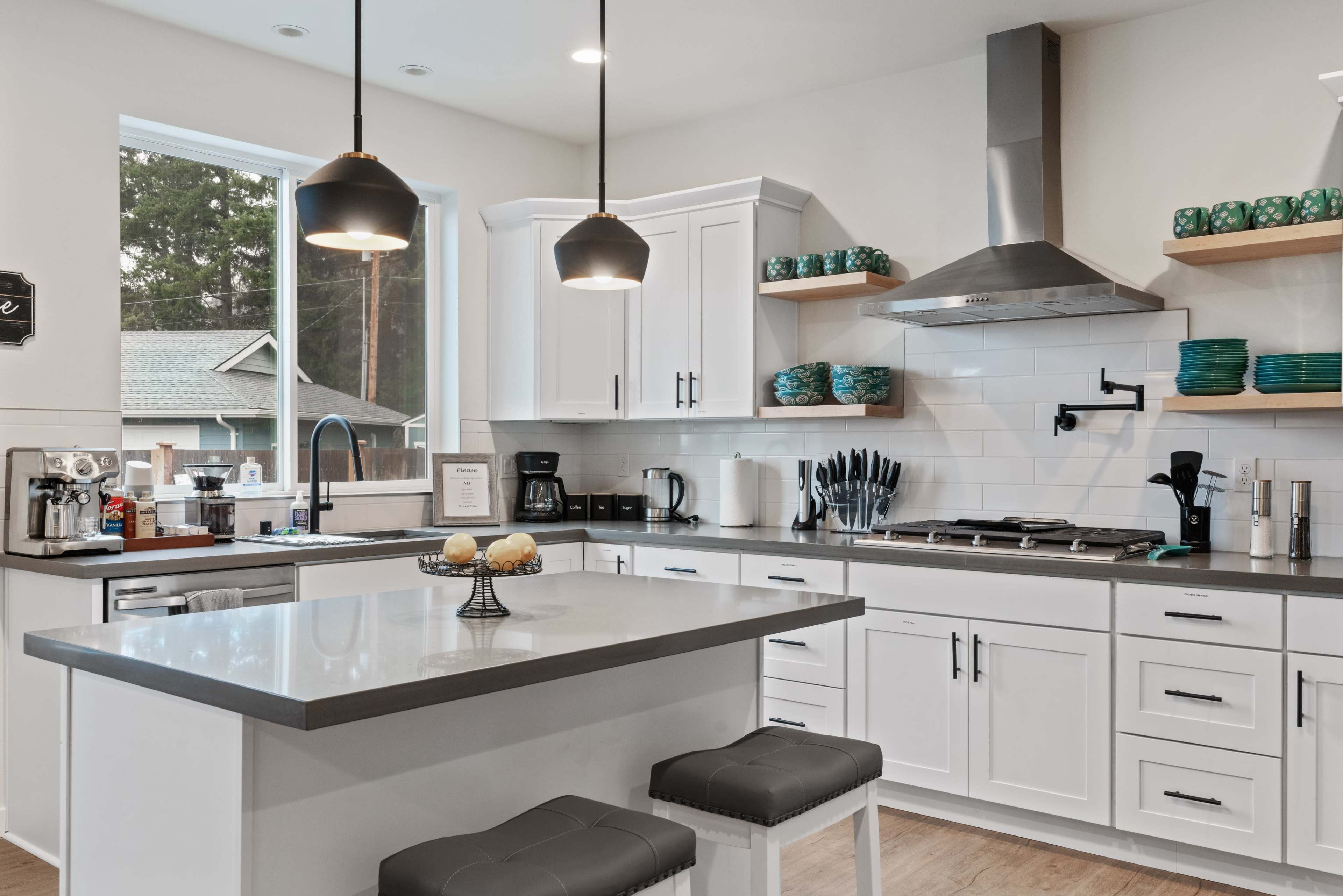 The kitchen features white cabinets, a gray island with stools, and stainless steel appliances, illuminated by pendant lights.