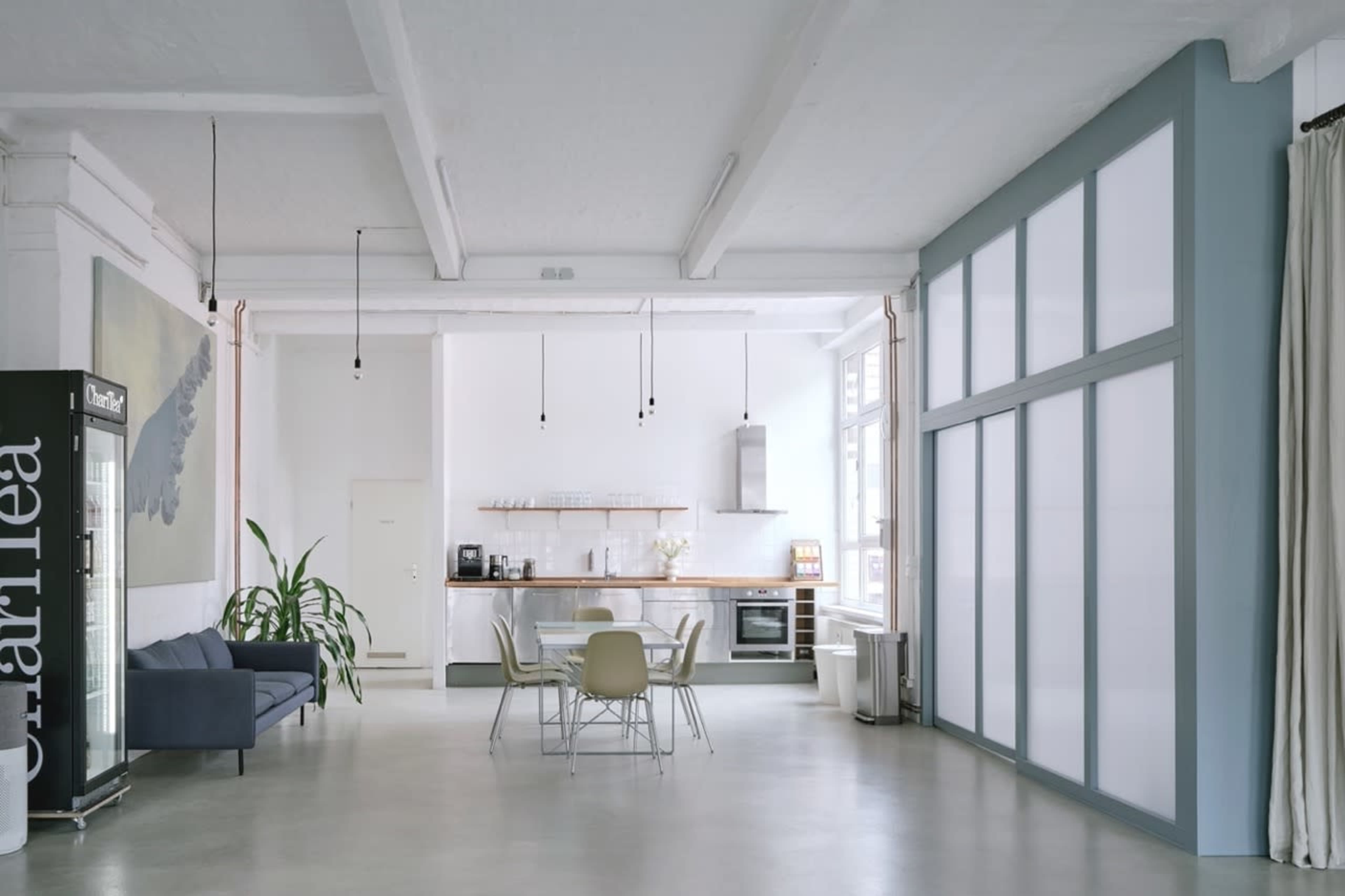 The image shows a spacious, modern interior featuring a kitchen area with wooden countertops and a dining table surrounded by chairs.
