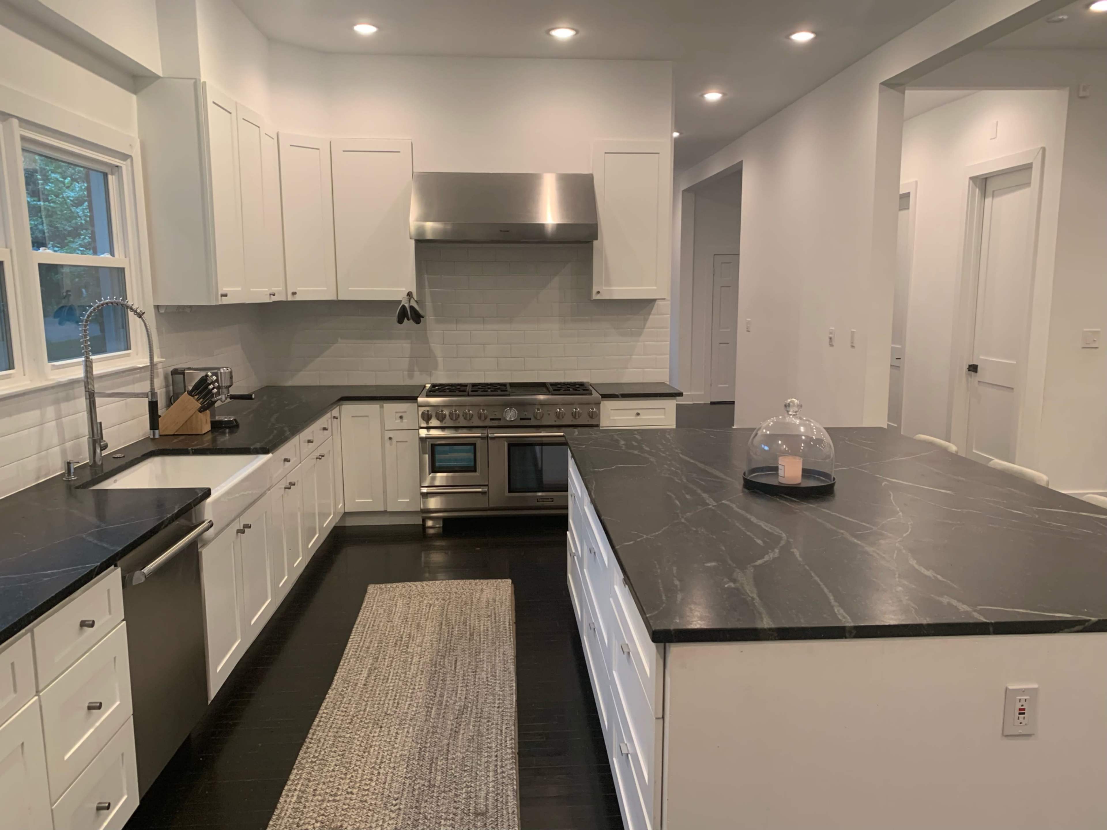 A modern kitchen featuring white cabinetry, a stainless steel range hood, and a dark marble countertop with a central island.