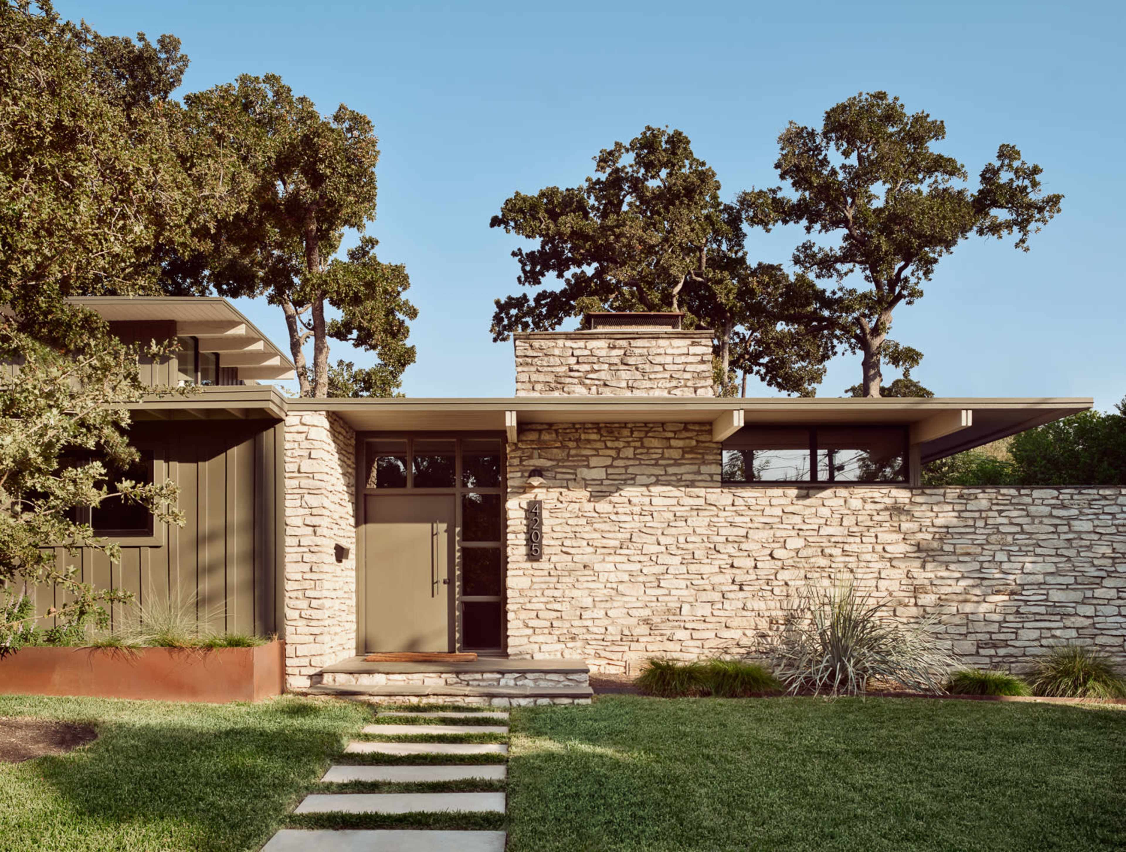 A modern house features a stone facade, flat rooflines, and a landscaped yard with stepping stones leading to the entrance.