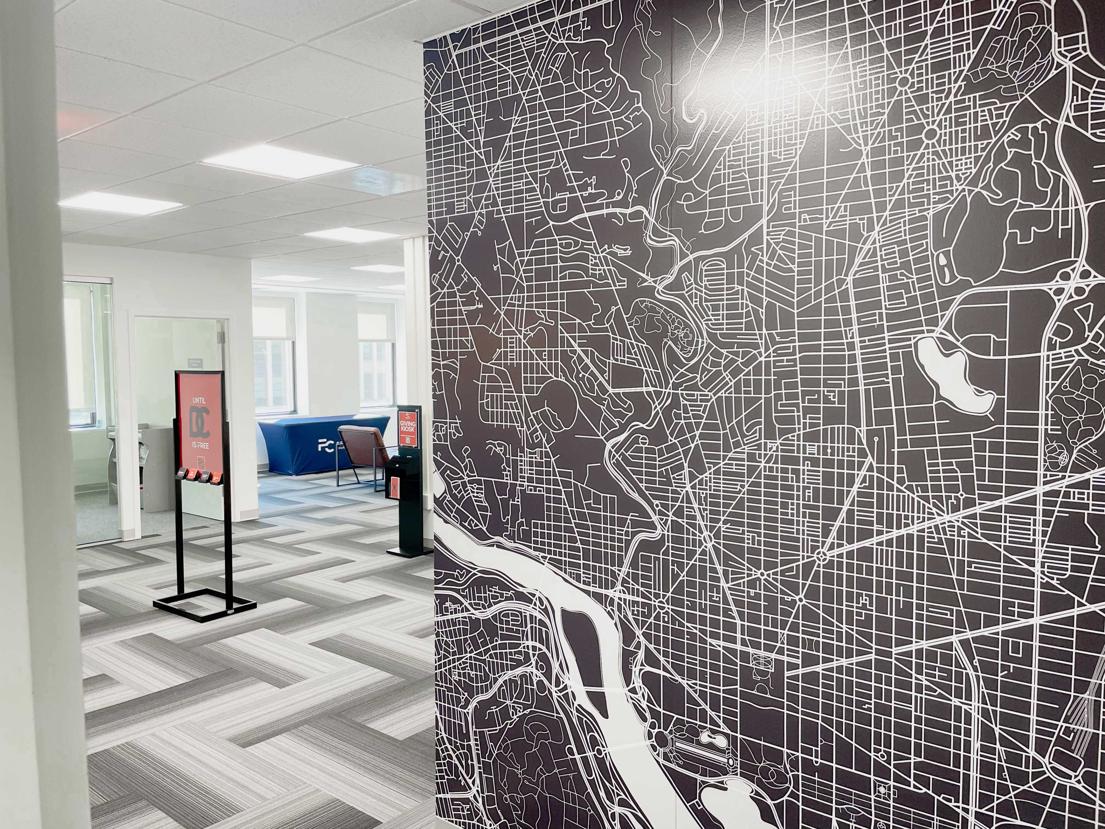 An office interior featuring a wall mural of a city map, with a corridor leading to workspaces in the background.