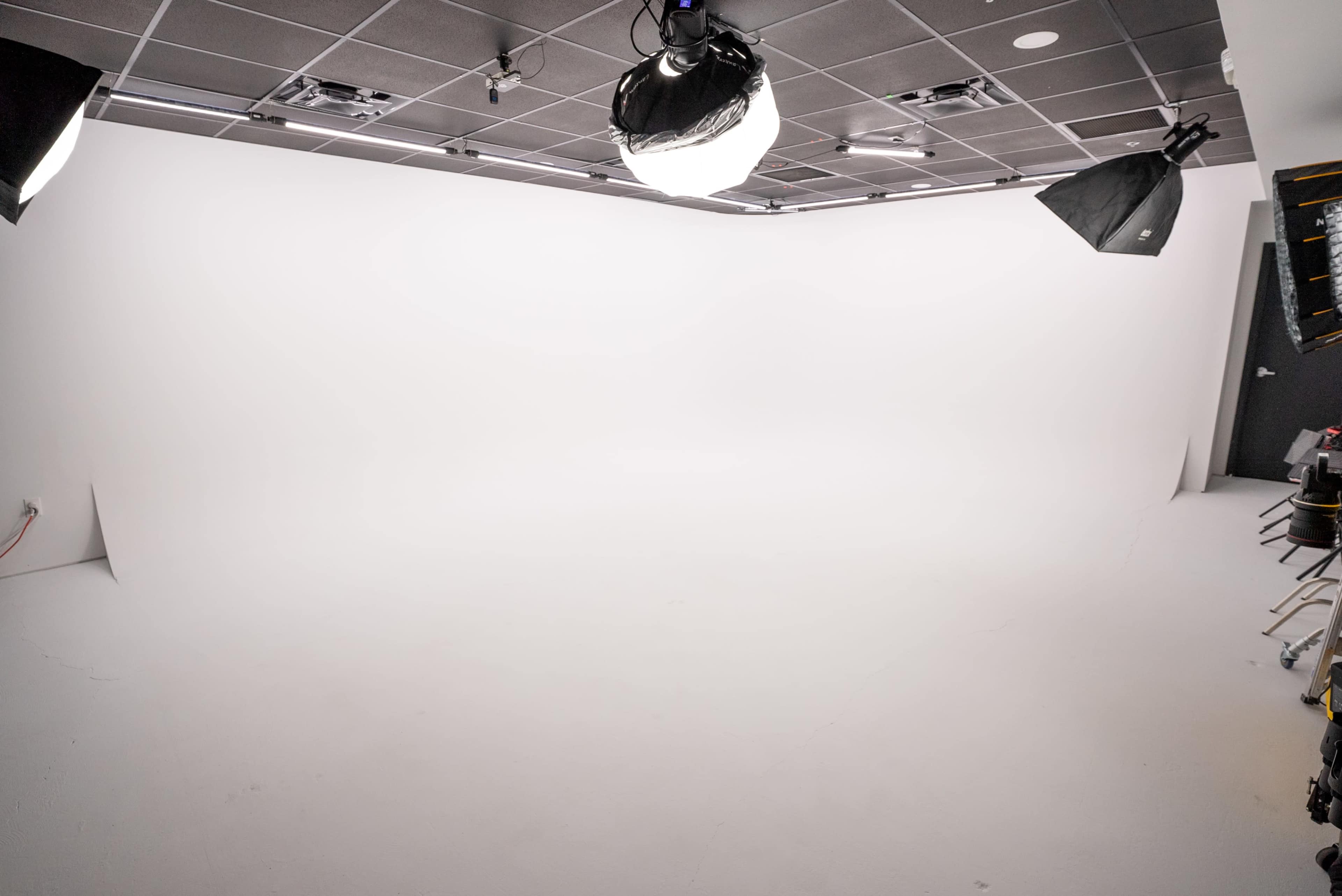 The image shows a studio space with a seamless white backdrop and multiple lighting fixtures positioned overhead.