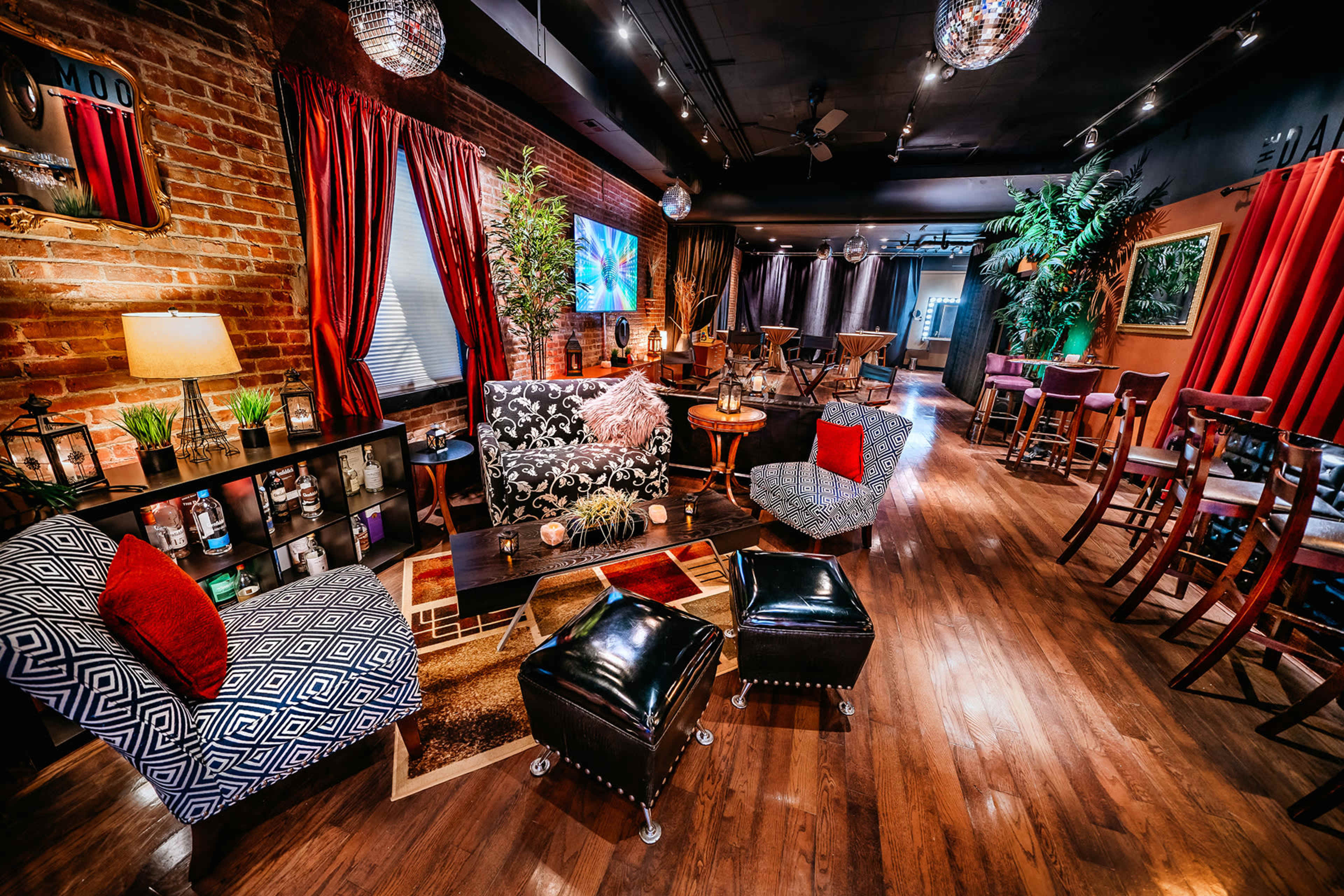 A cozy lounge area with brick walls, various seating arrangements, and decorative plants, illuminated by soft lighting and adorned with disco balls.