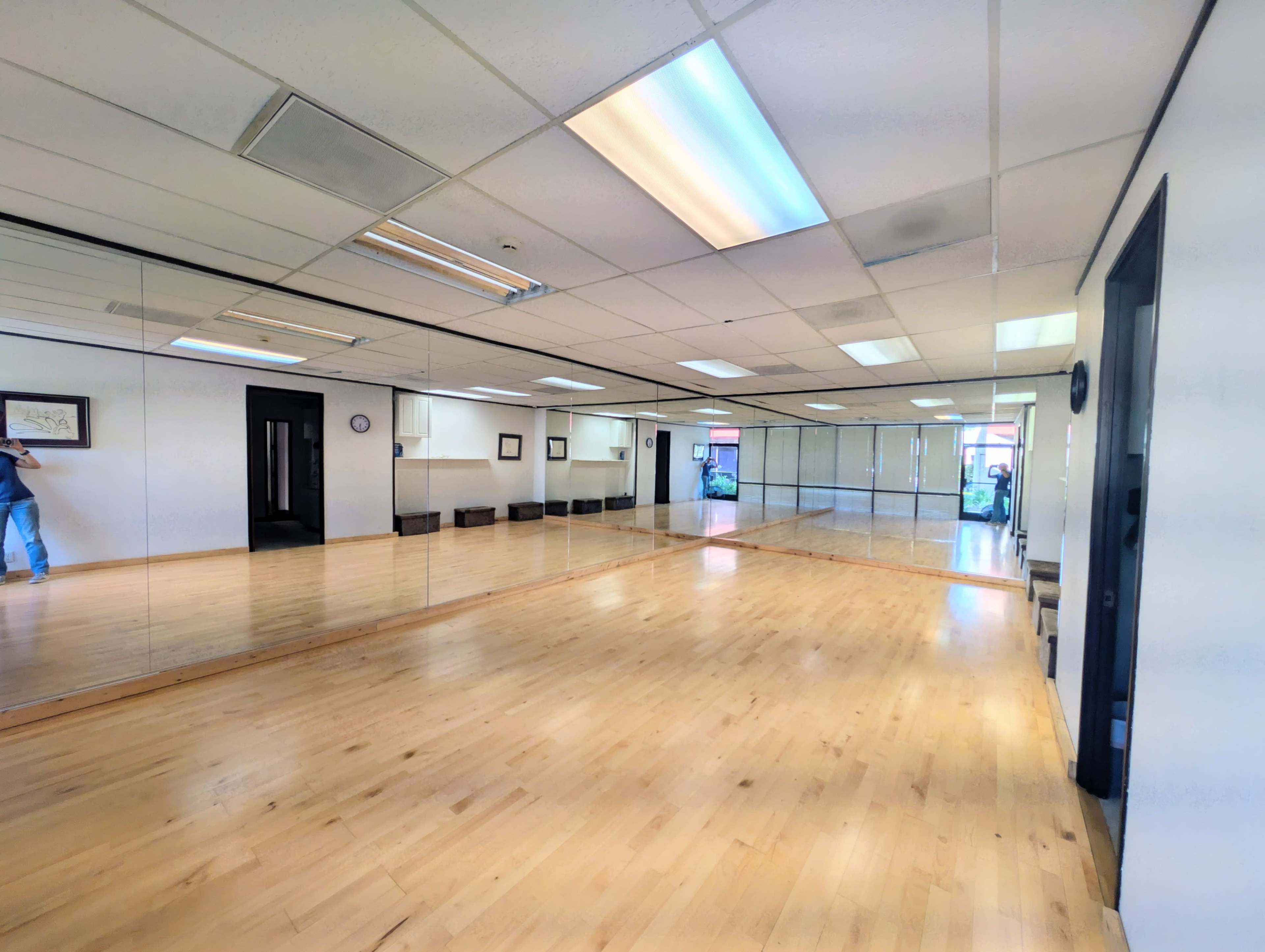 The image shows a spacious studio or exercise room with wooden flooring and mirrors covering one wall.