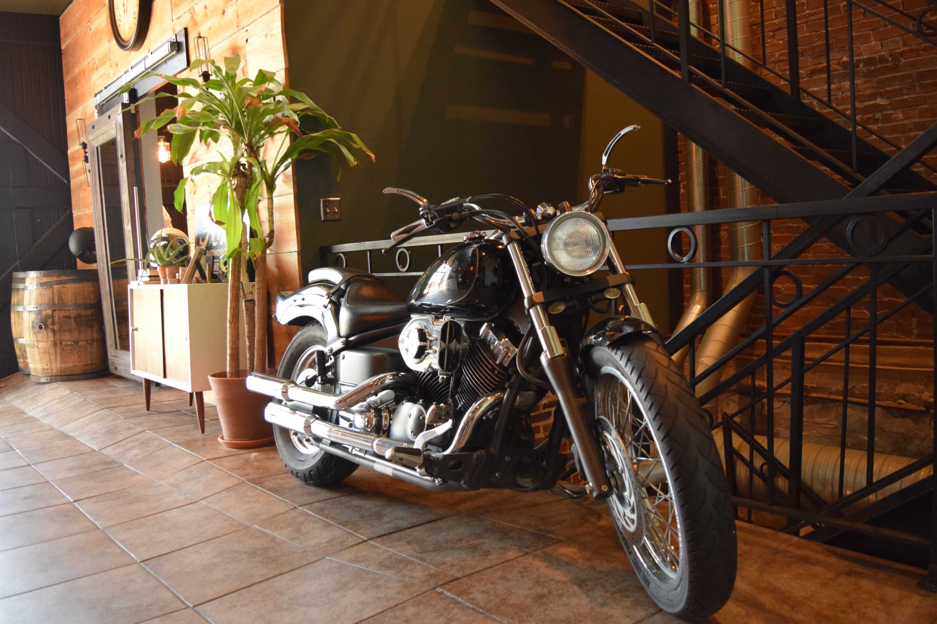 A motorcycle is parked next to a plant and a wooden cabinet in a brick-walled interior space.