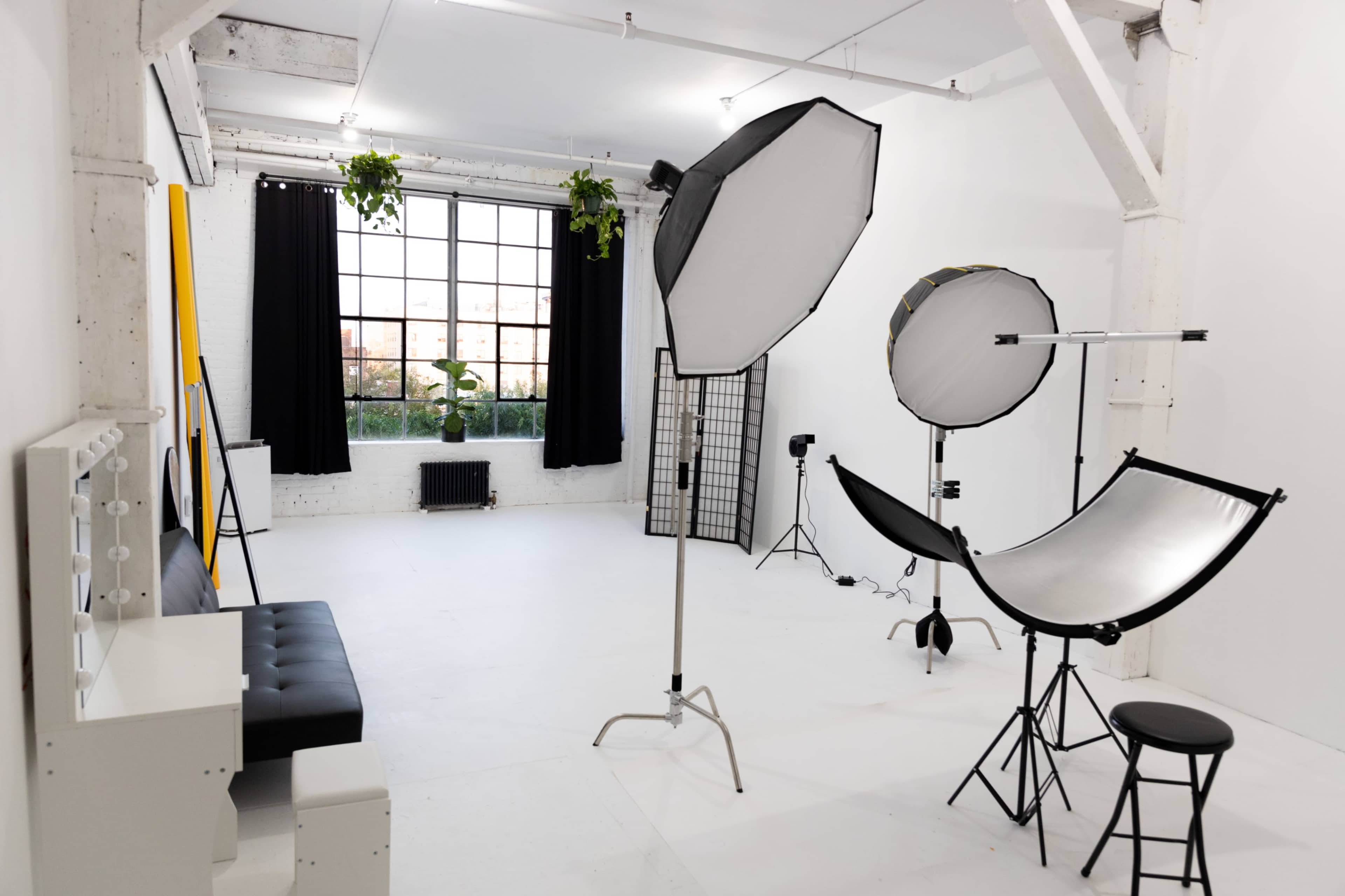 The image shows a photography studio featuring backdrop stands, light sources, and a seating area with a mirror.